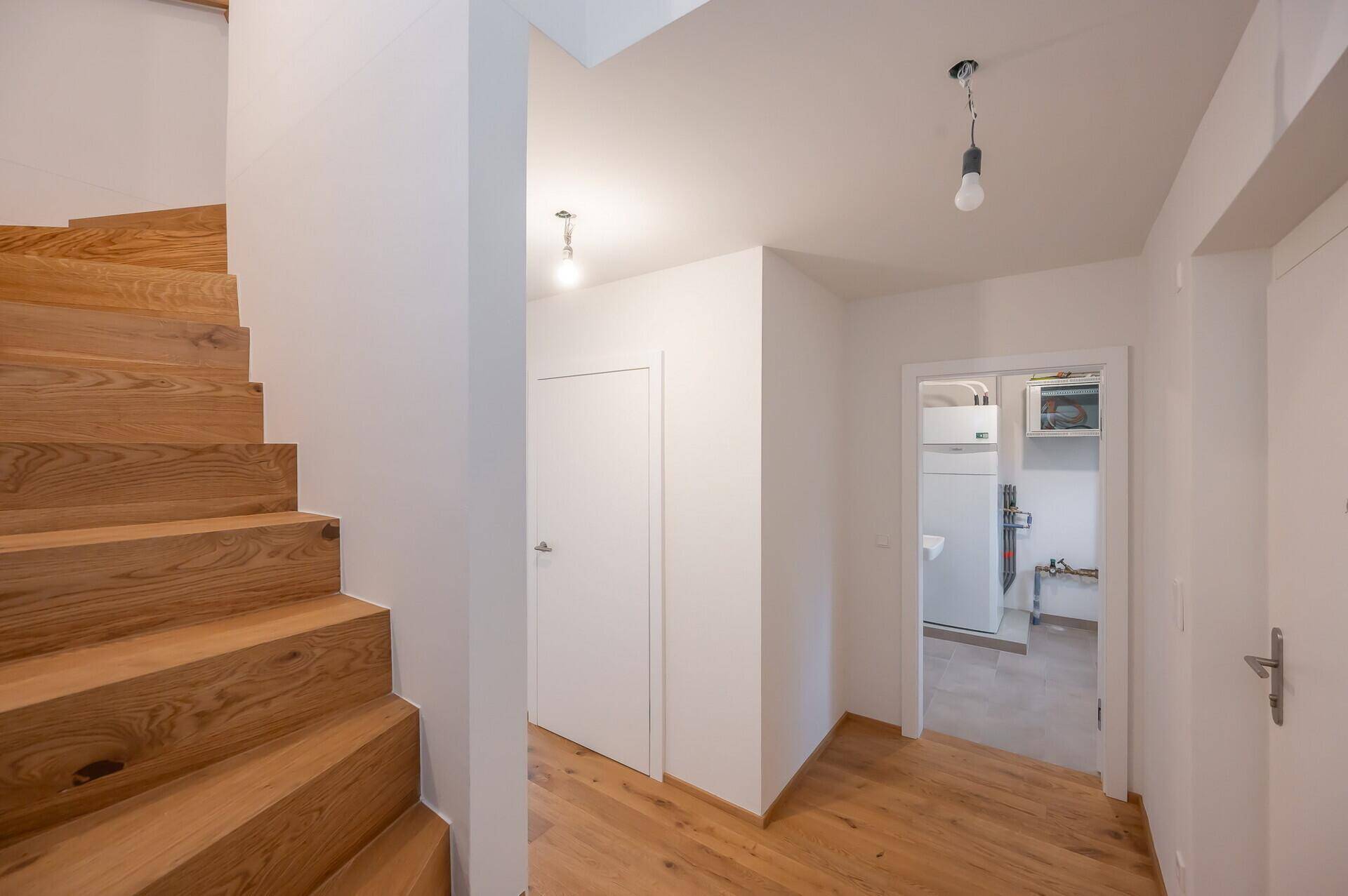 Heller Flur mit Holztreppe und Zugang zum Hauswirtschaftsraum.
