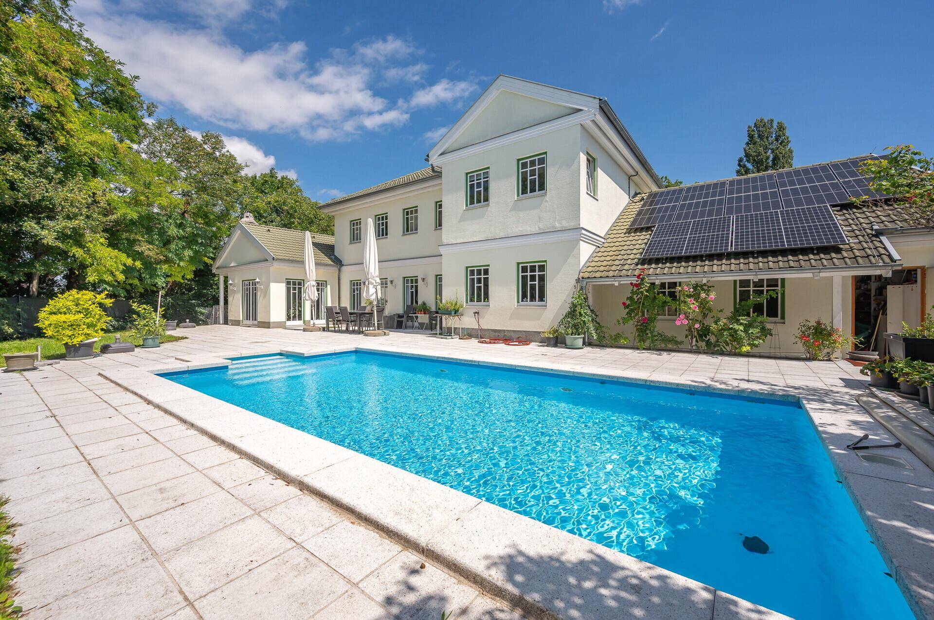 Außenbereich mit großem Pool, Sonnenterrasse und Photovoltaikanlage auf dem Dach.
