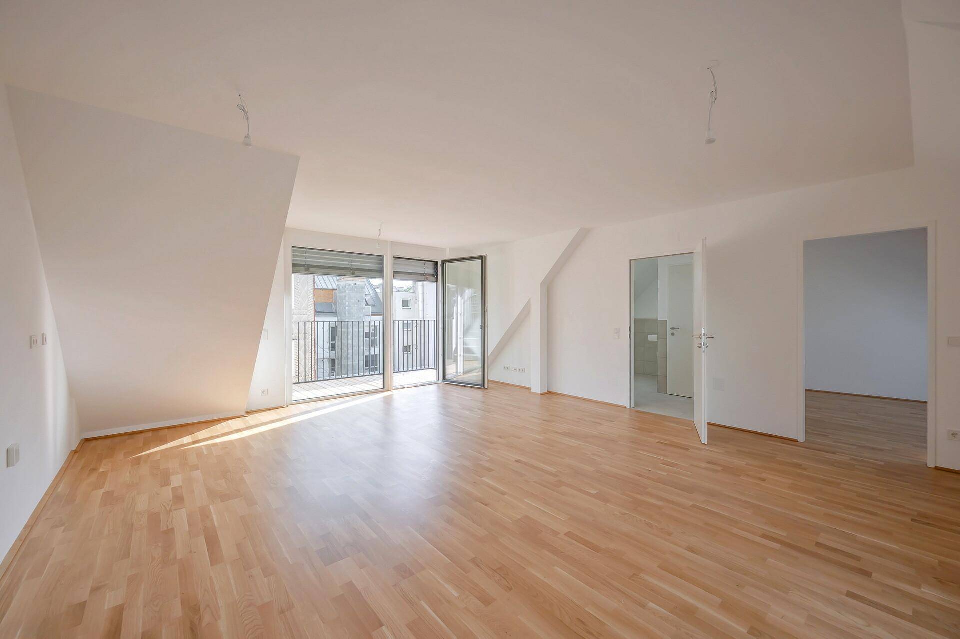 Helles Wohnzimmer mit Parkettboden, Dachschrägen und Zugang zu einem französischen Balkon.