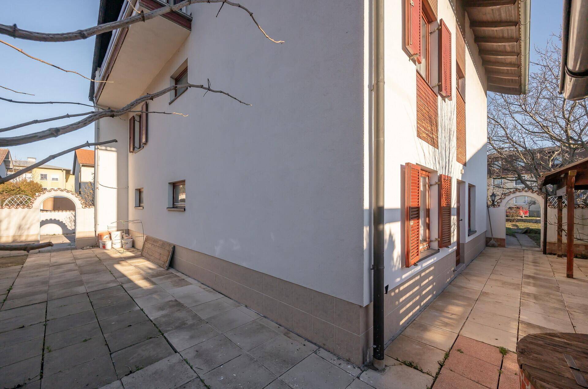 Seitenansicht des Hauses mit gepflastertem Weg und sonnigem Außenbereich unter blauem Himmel.