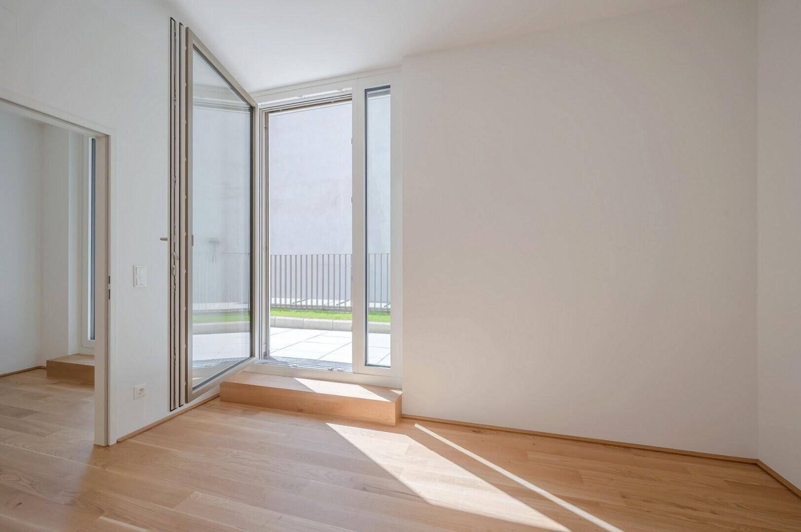 Lichtdurchfluteter Raum mit Holzboden und Zugang zu einem sonnigen Außenbereich.