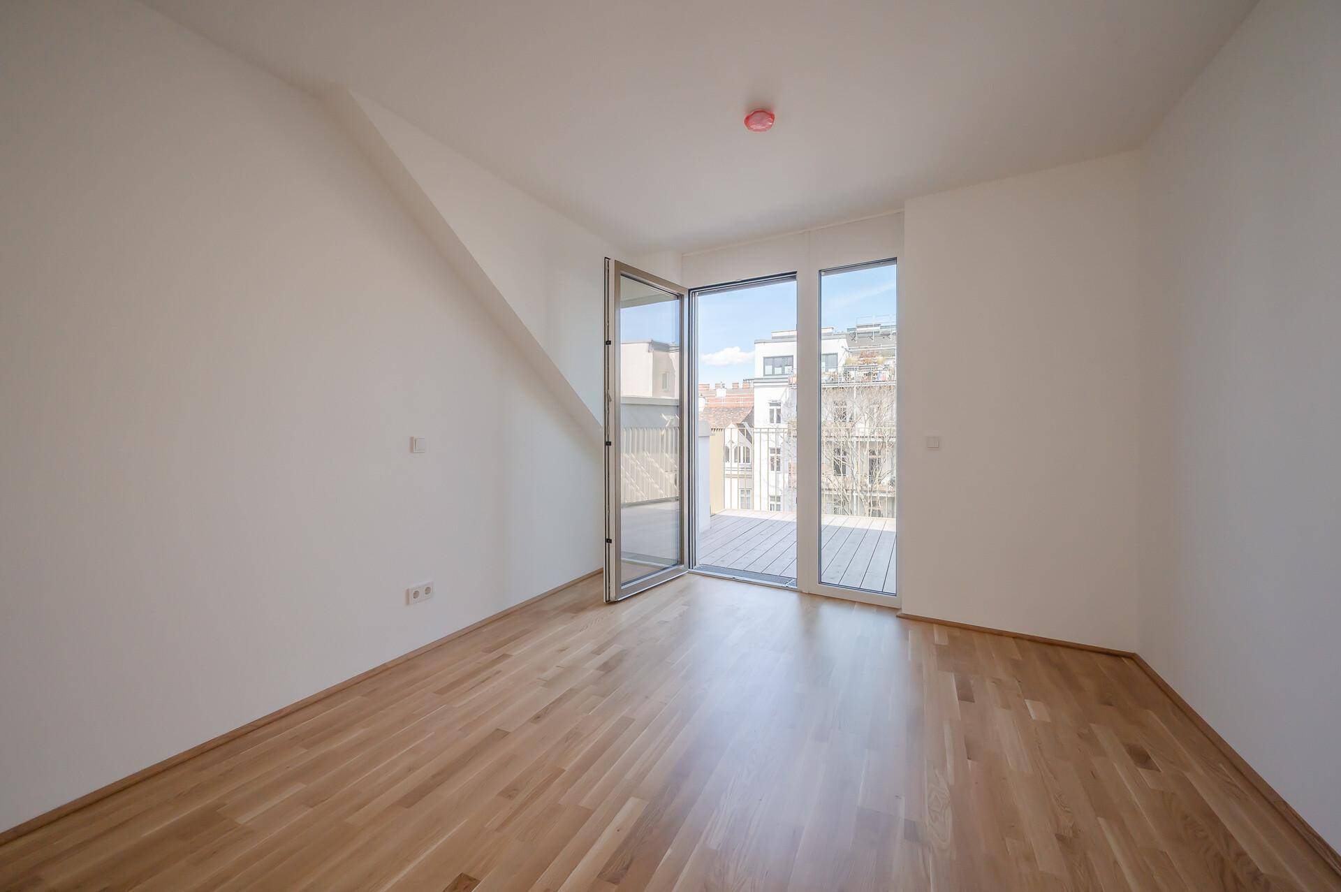 Helles Zimmer mit Parkettboden und schrägen Wänden, das Zugang zu einem Außenbereich bietet.
