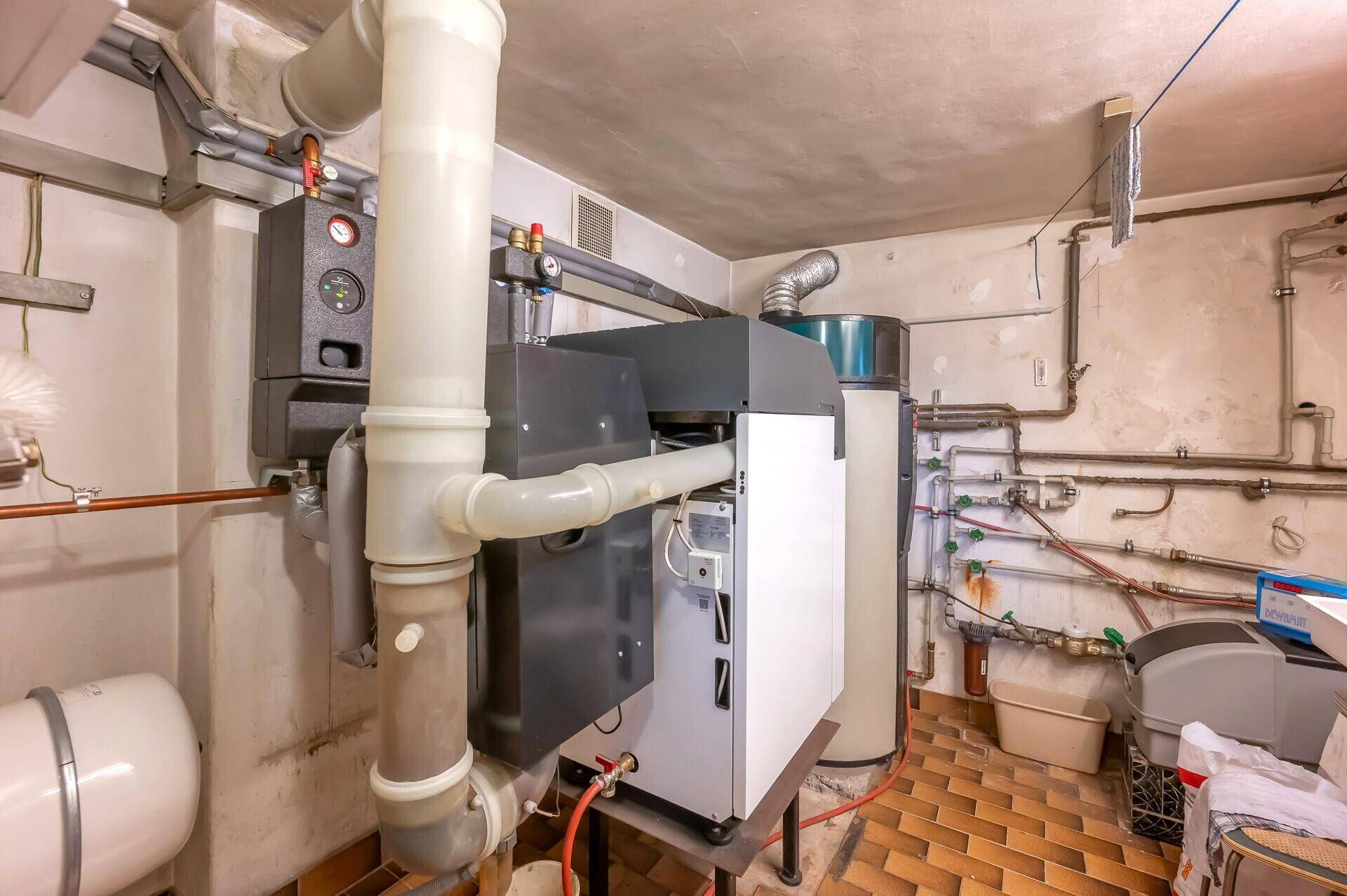 Heizungsraum mit moderner Heizungsanlage, Warmwasserspeicher und sichtbaren Leitungen.