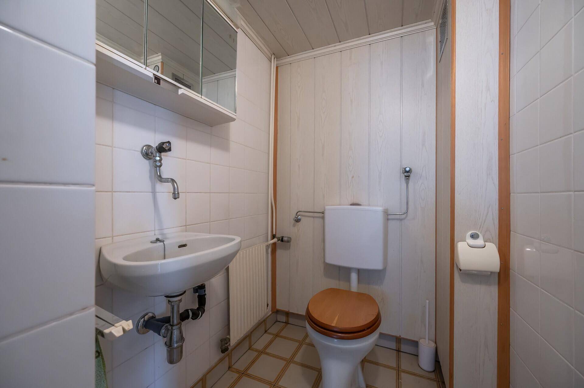 Kleines WC mit Waschbecken, Toilette und gefliesten Wänden in schlichtem Design.