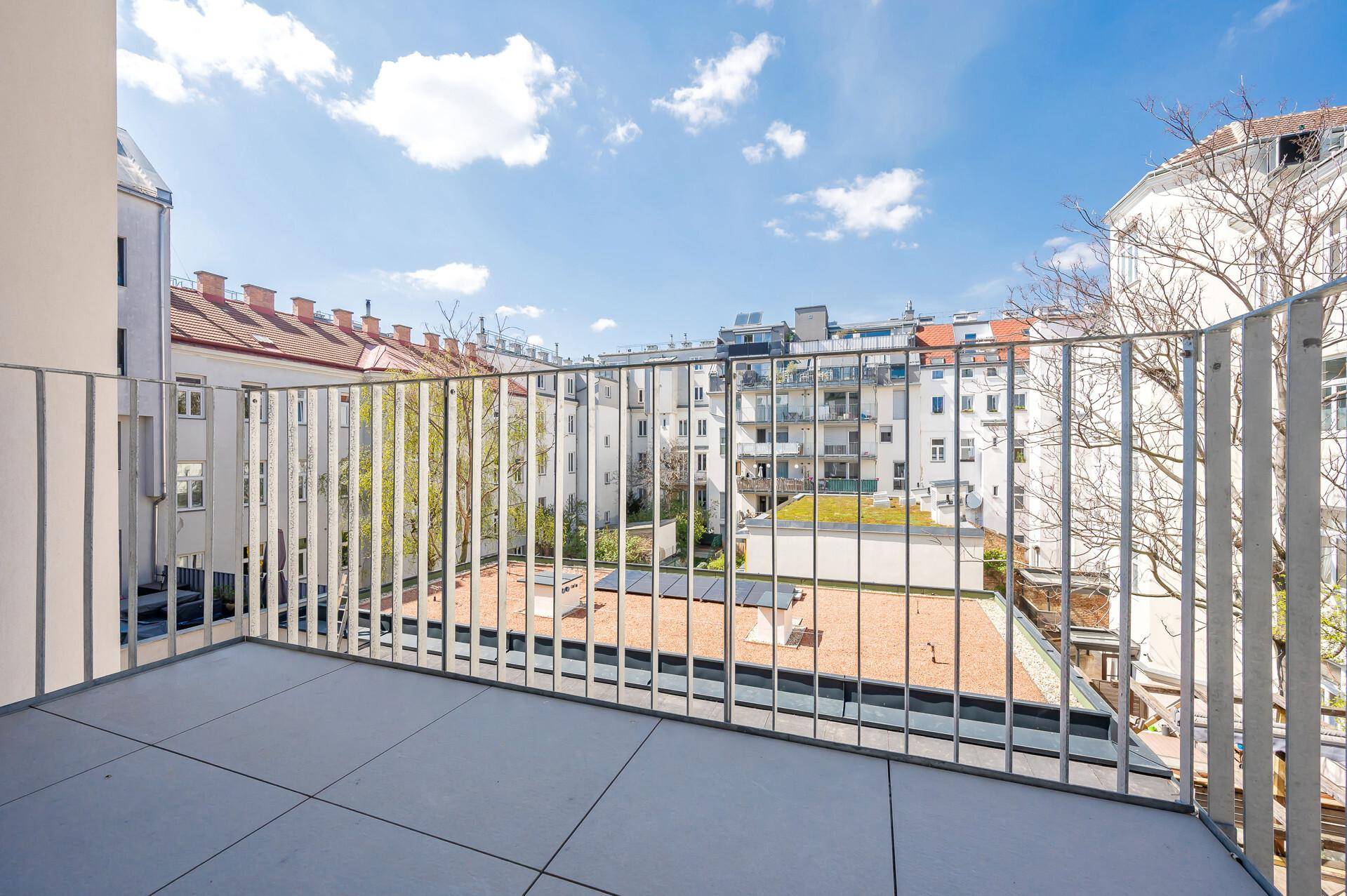 Geräumiger Balkon mit Metallgeländer und Blick auf umliegende Wohngebäude und Dächer.
