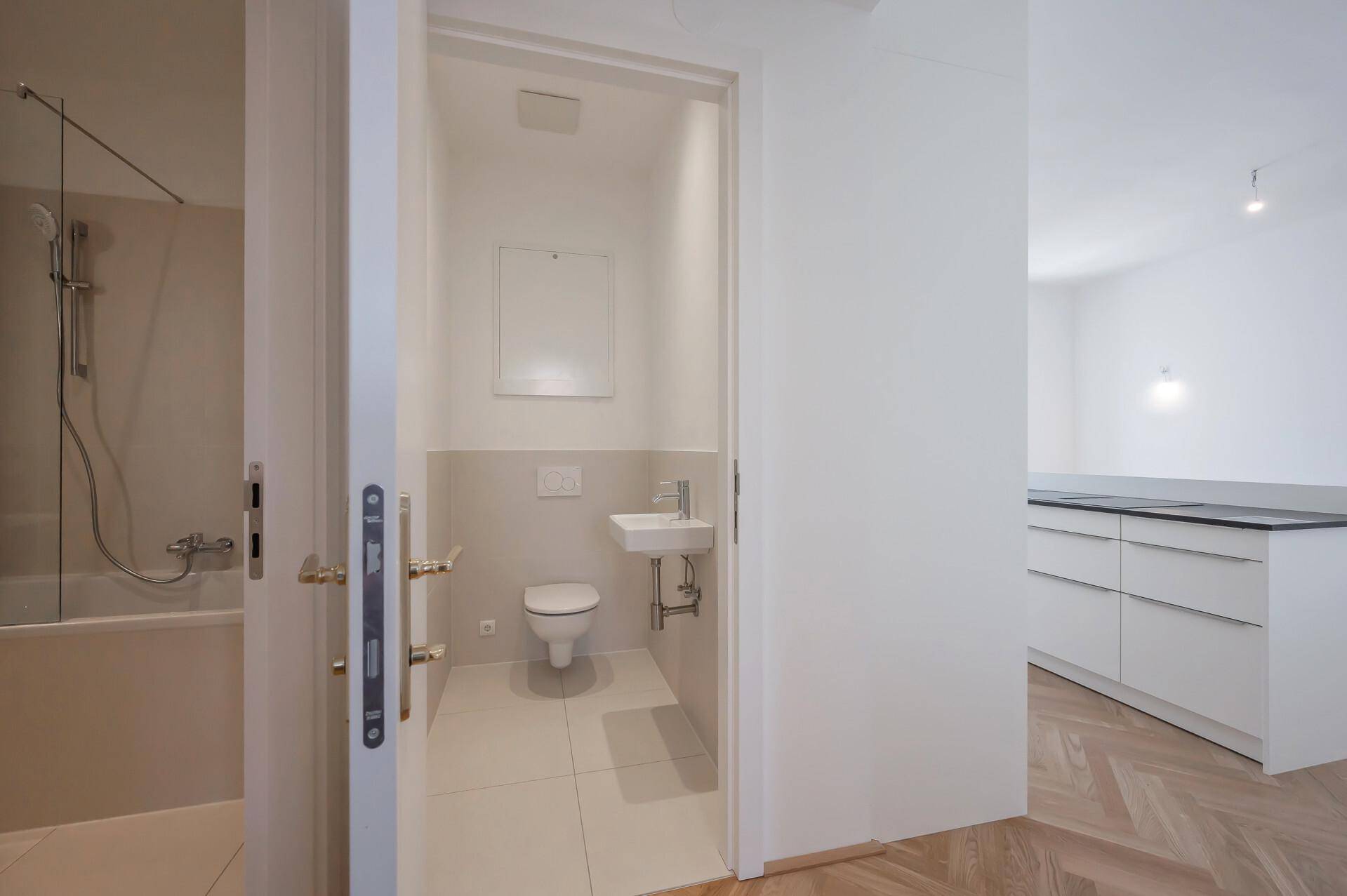 Blick in eine moderne Gästetoilette mit wandhängendem WC und kleinem Waschbecken, angrenzend an ein Badezimmer.