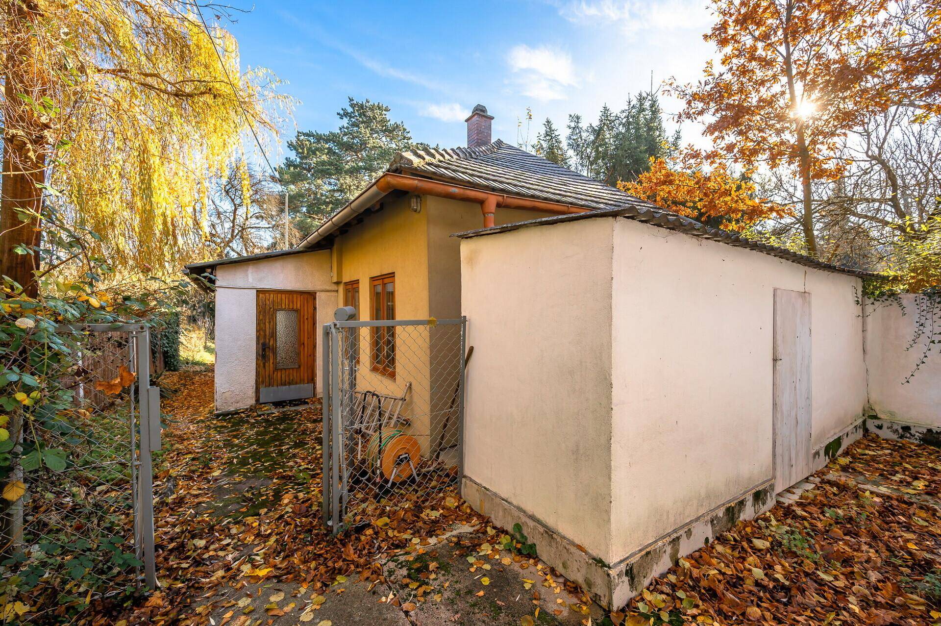 Seitenansicht des Hauses mit Anbau und kleinem Schuppen, umgeben von herbstlichem Laub.