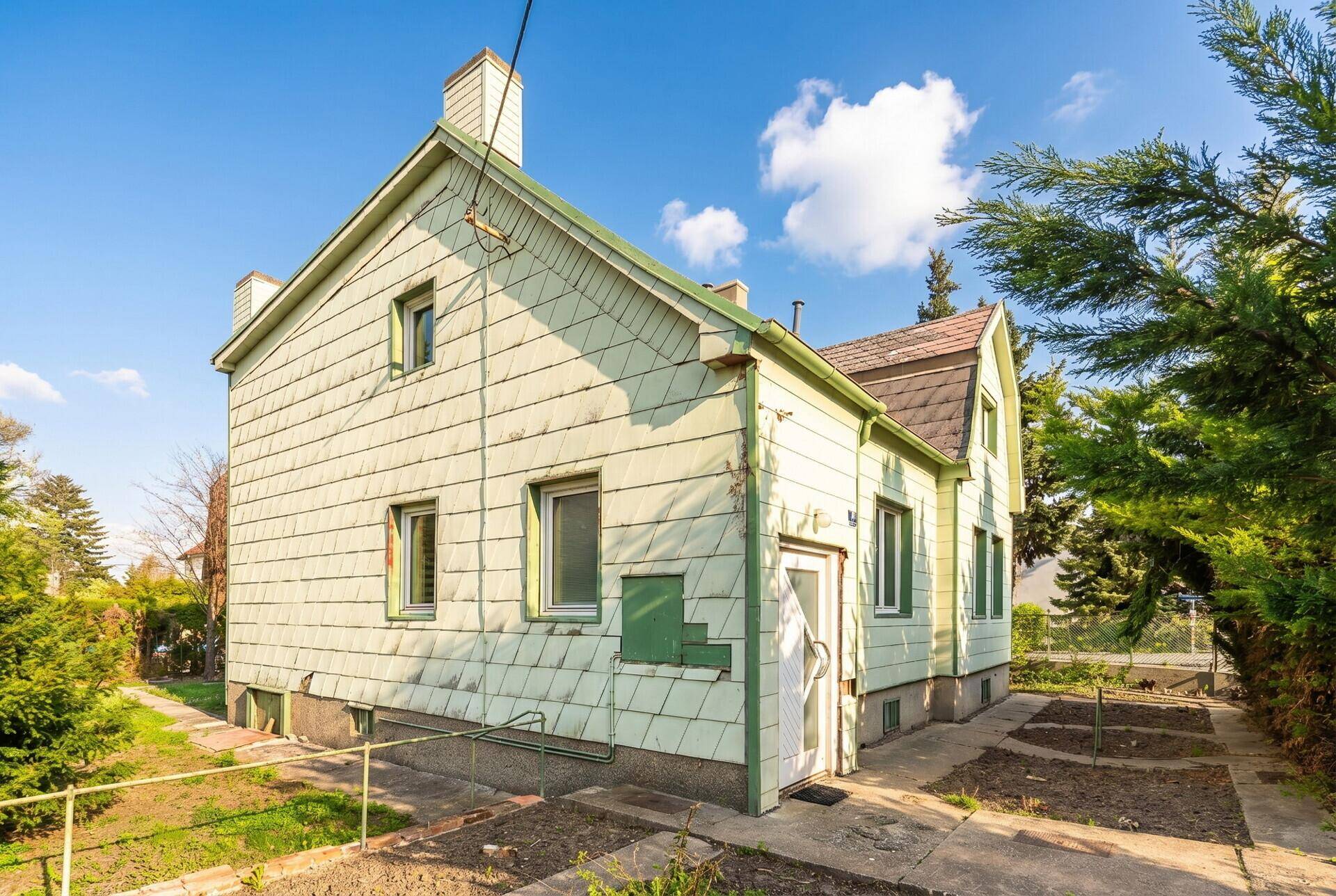 Seitenansicht des Hauses mit Gartenbereich und Eingangstür, umgeben von Bäumen.