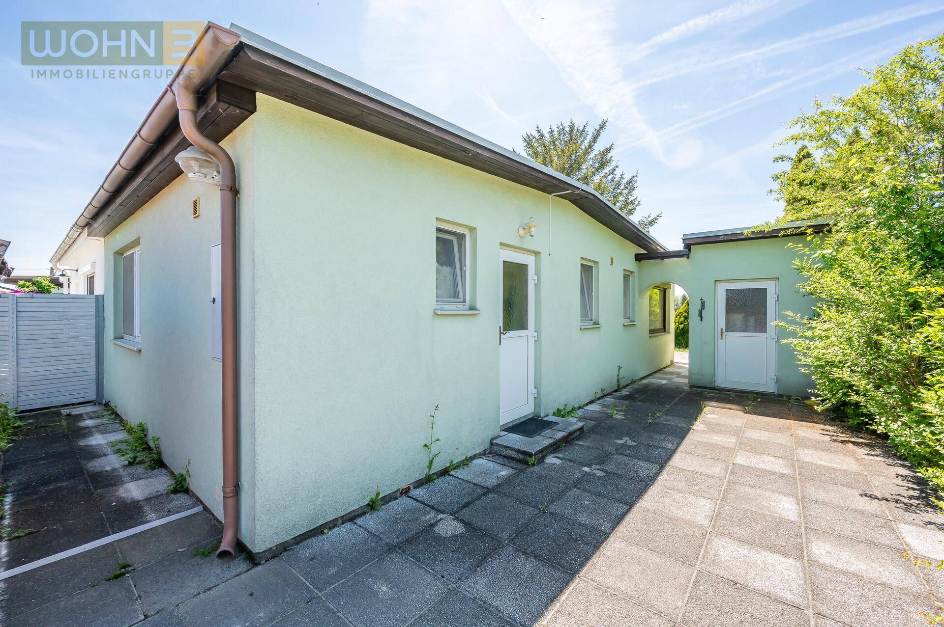 Seitenansicht des Hauses mit gepflastertem Zugang und einem kleinen Anbau.