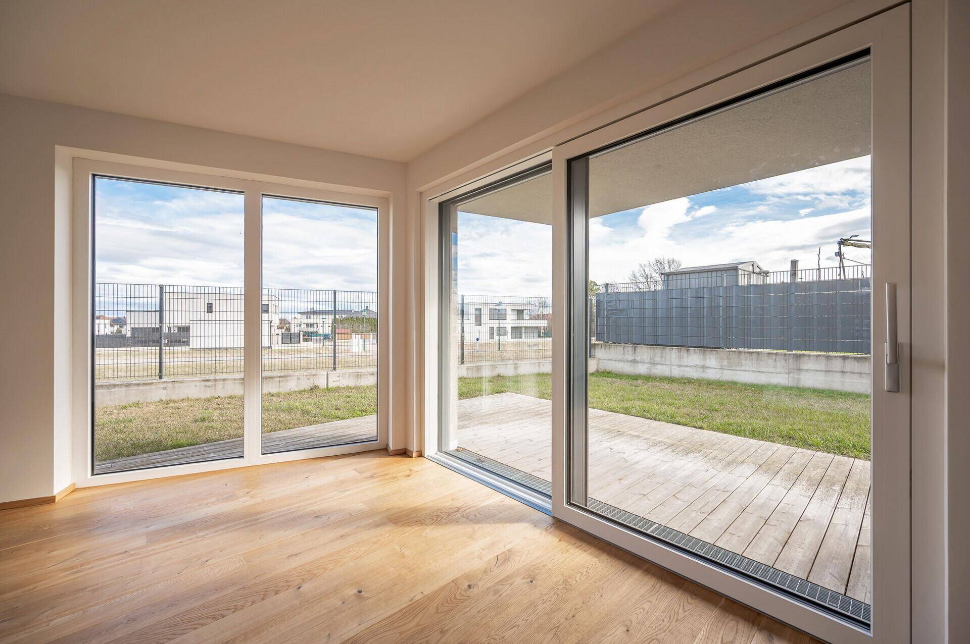 Heller Wohnraum mit weitem Blick in den Garten und auf die Holzterrasse durch große Fenster.