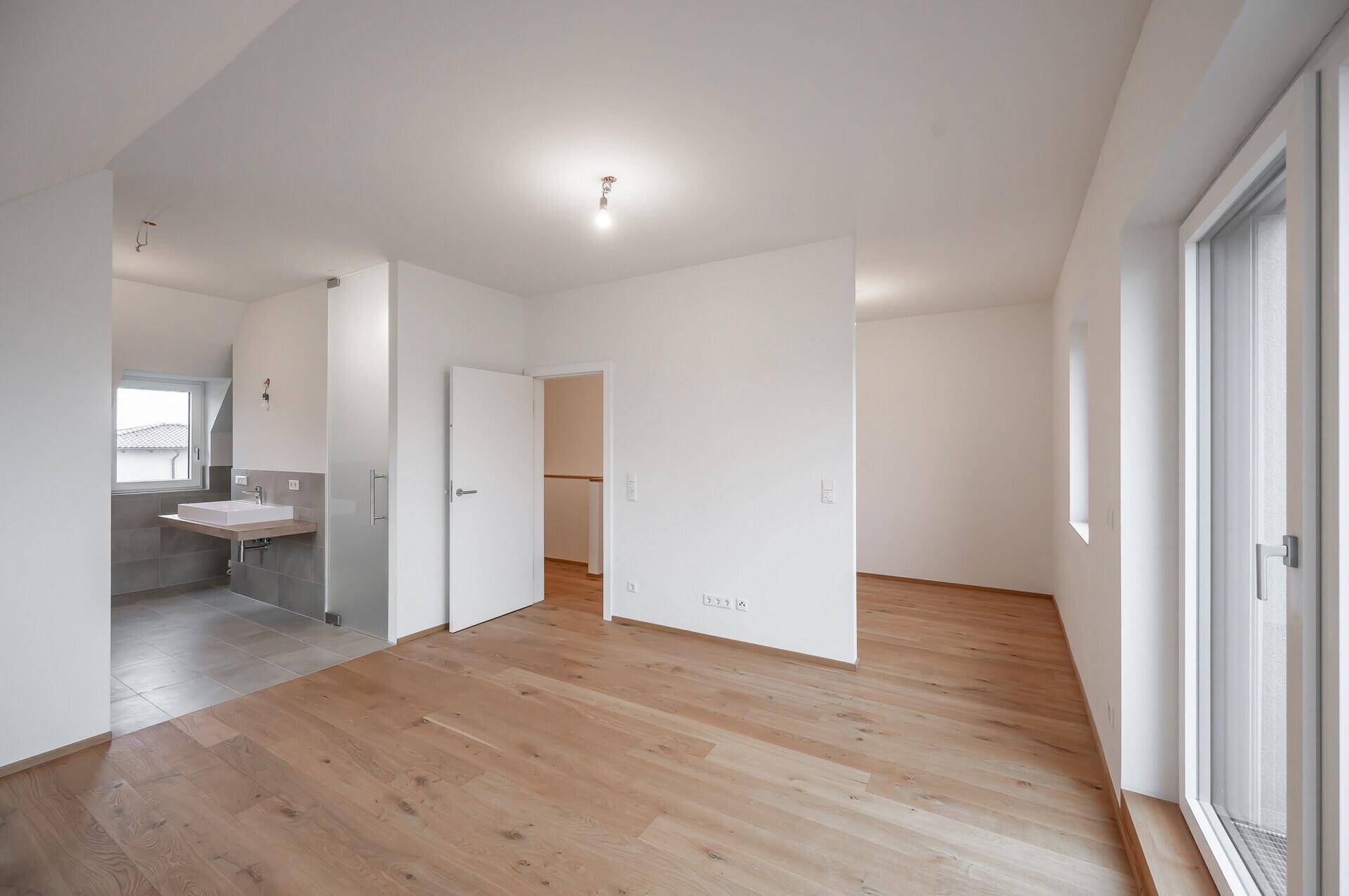 Geräumiges Schlafzimmer im Dachgeschoss mit Holzboden und direktem Zugang zum Badezimmer.
