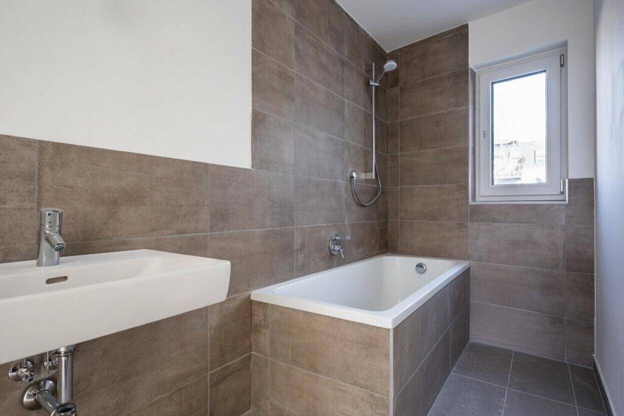 Modernes Badezimmer mit Badewanne, Waschbecken und Fenster, ausgestattet mit braunen Fliesen.