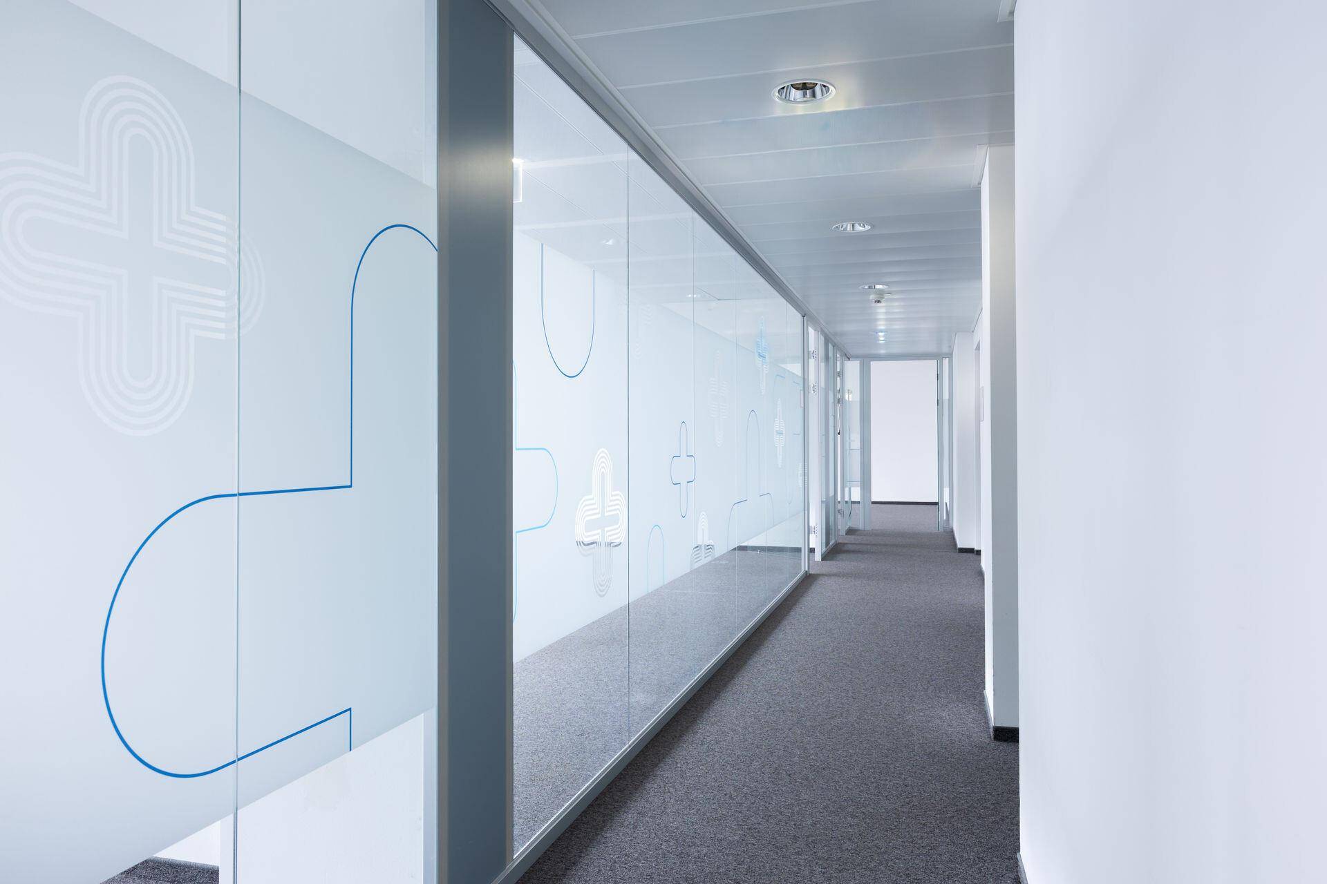 Moderner Bürogang mit durchgehenden Glaswänden und dezenten Mustern, die für Privatsphäre sorgen.
