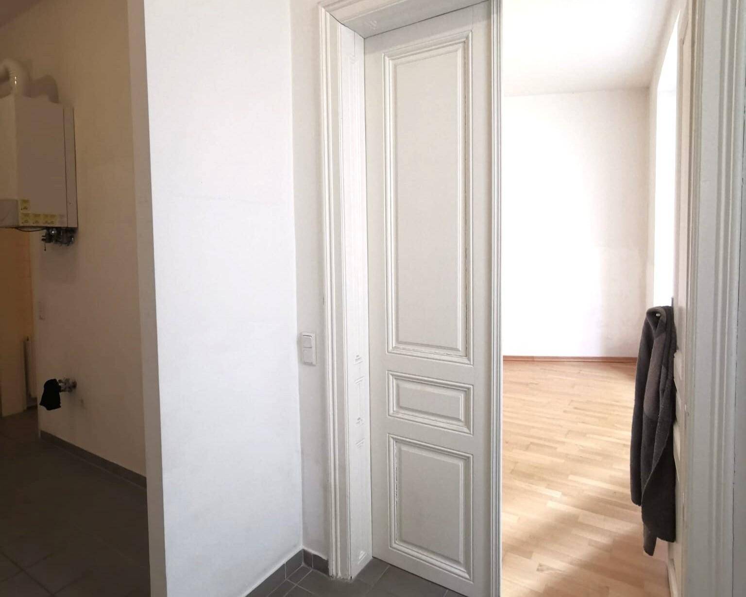 Offene Tür führt von einem gefliesten Bereich in einen hellen Raum mit Holzfußboden.