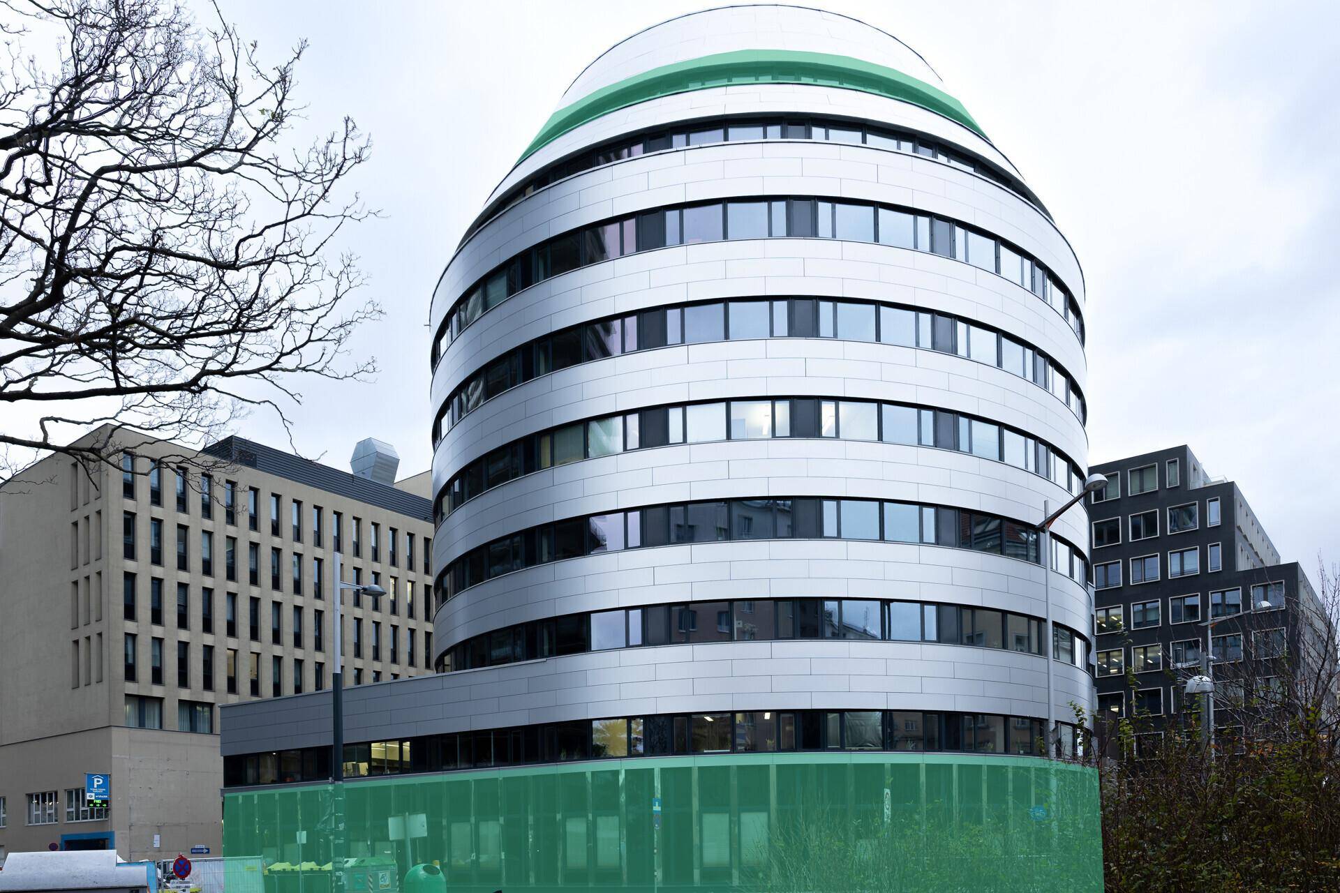 Modernes, geschwungenes Gebäude mit vielen Fenstern und einer auffälligen Fassadengestaltung in urbaner Umgebung.