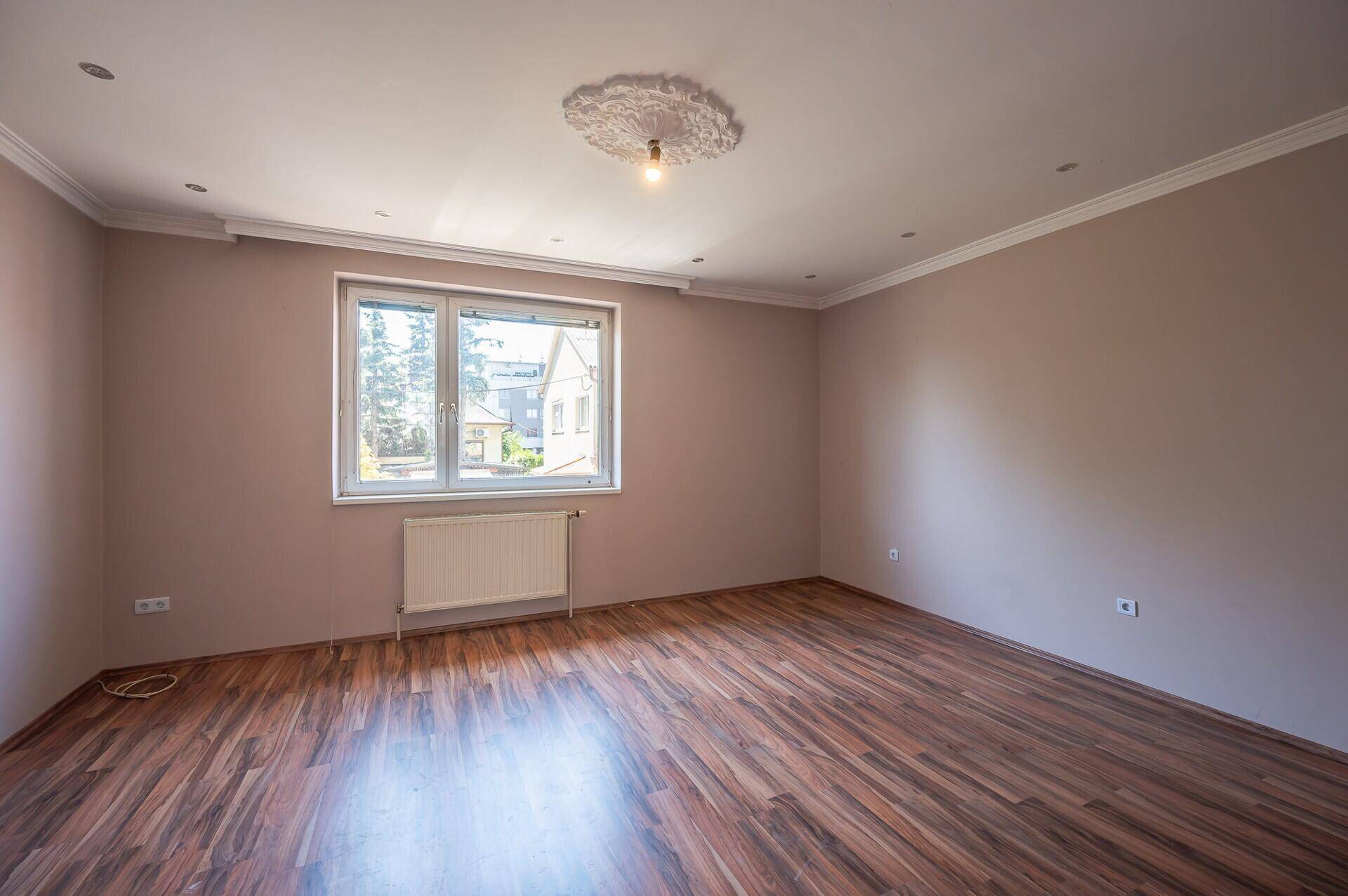 Schlafzimmer mit Laminatboden, beigen Wänden und einem Fenster mit Blick nach draußen.
