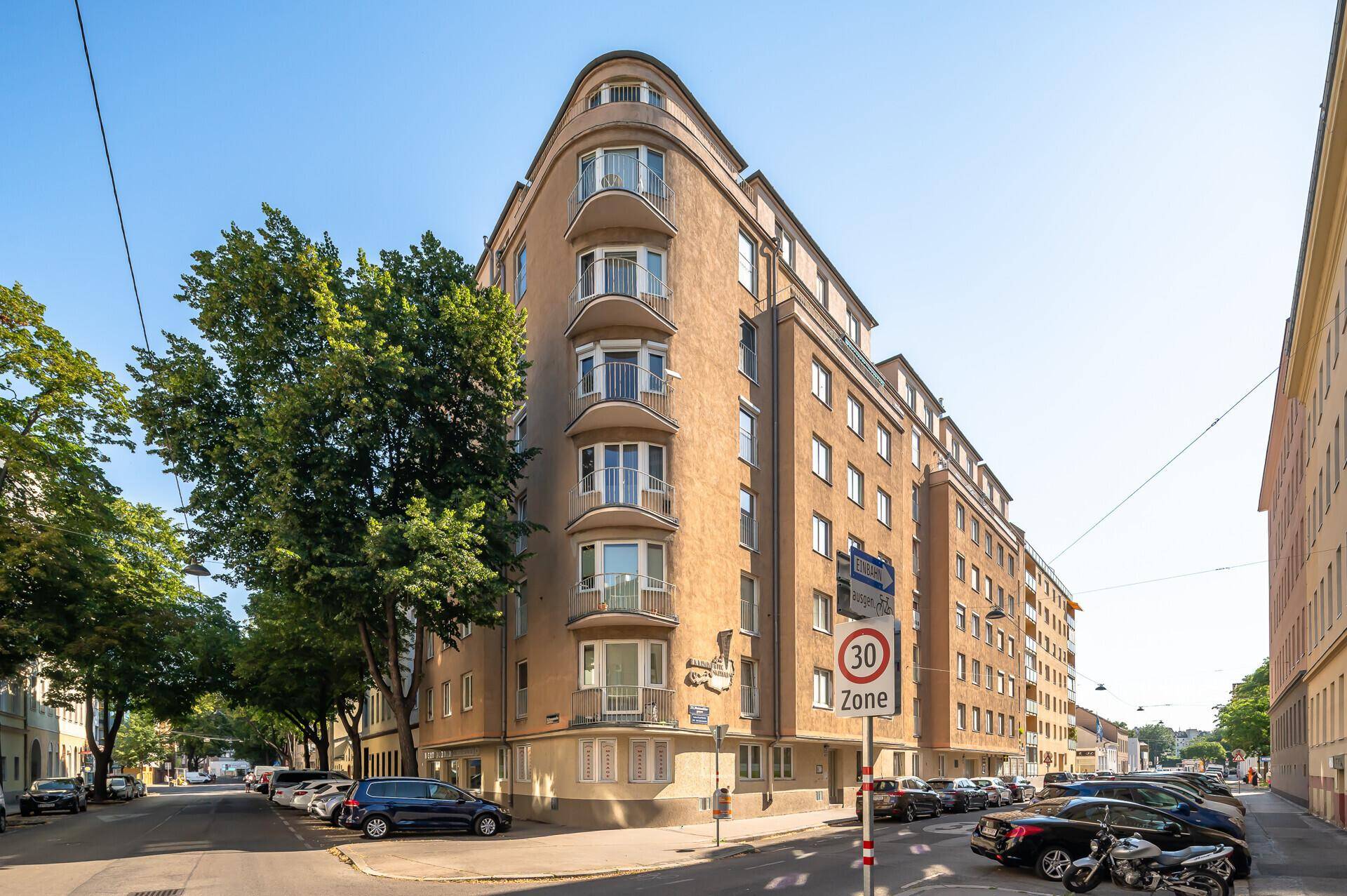 Historisches Eckgebäude mit abgerundeter Fassade und Balkonen an einer Straße.