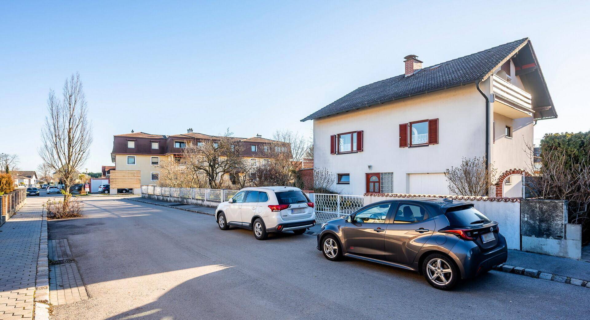 Ruhige Wohnstraße mit geparkten Autos und Einfamilienhäusern unter blauem Himmel.