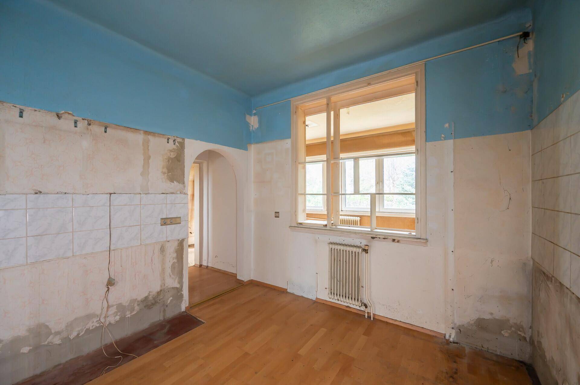 Renovierungsbedürftige Küche mit blauer Decke, Heizkörper und Fenster.