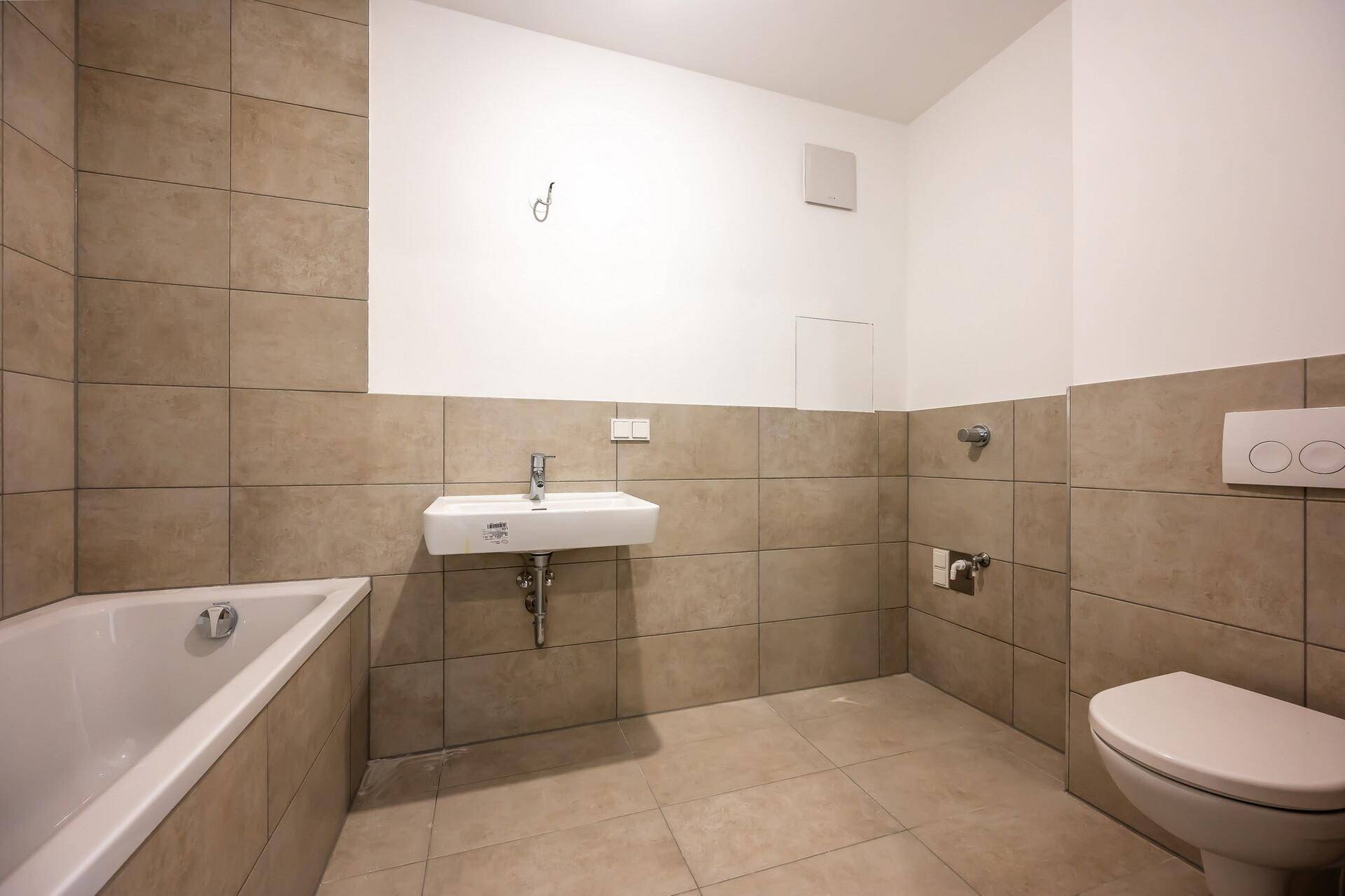 Modernes Badezimmer mit Badewanne, Waschbecken und Wand-WC, gefliest in neutralen Farbtönen.