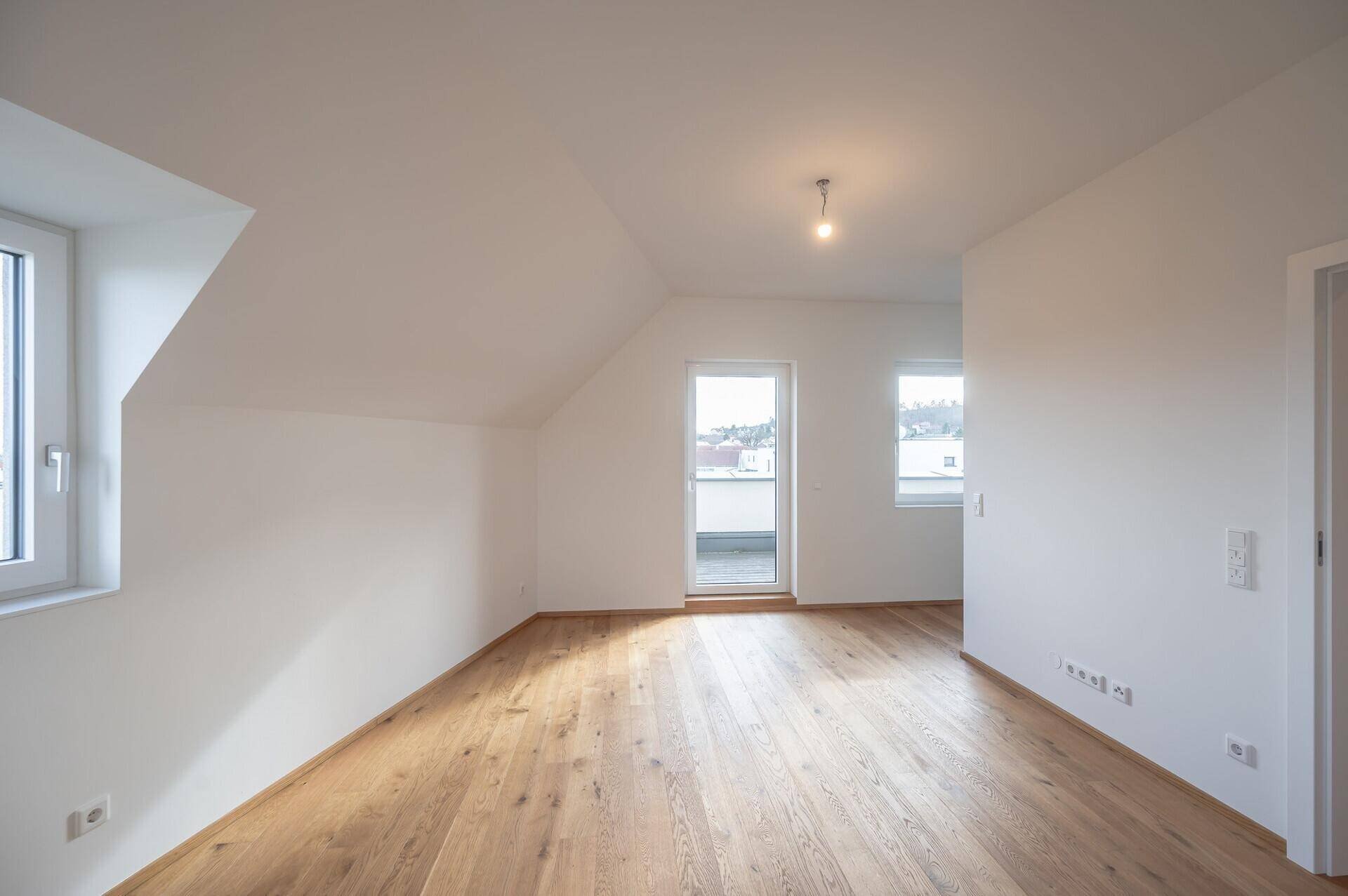 Helles Schlafzimmer im Dachgeschoss mit Holzboden und Zugang zur Dachterrasse.