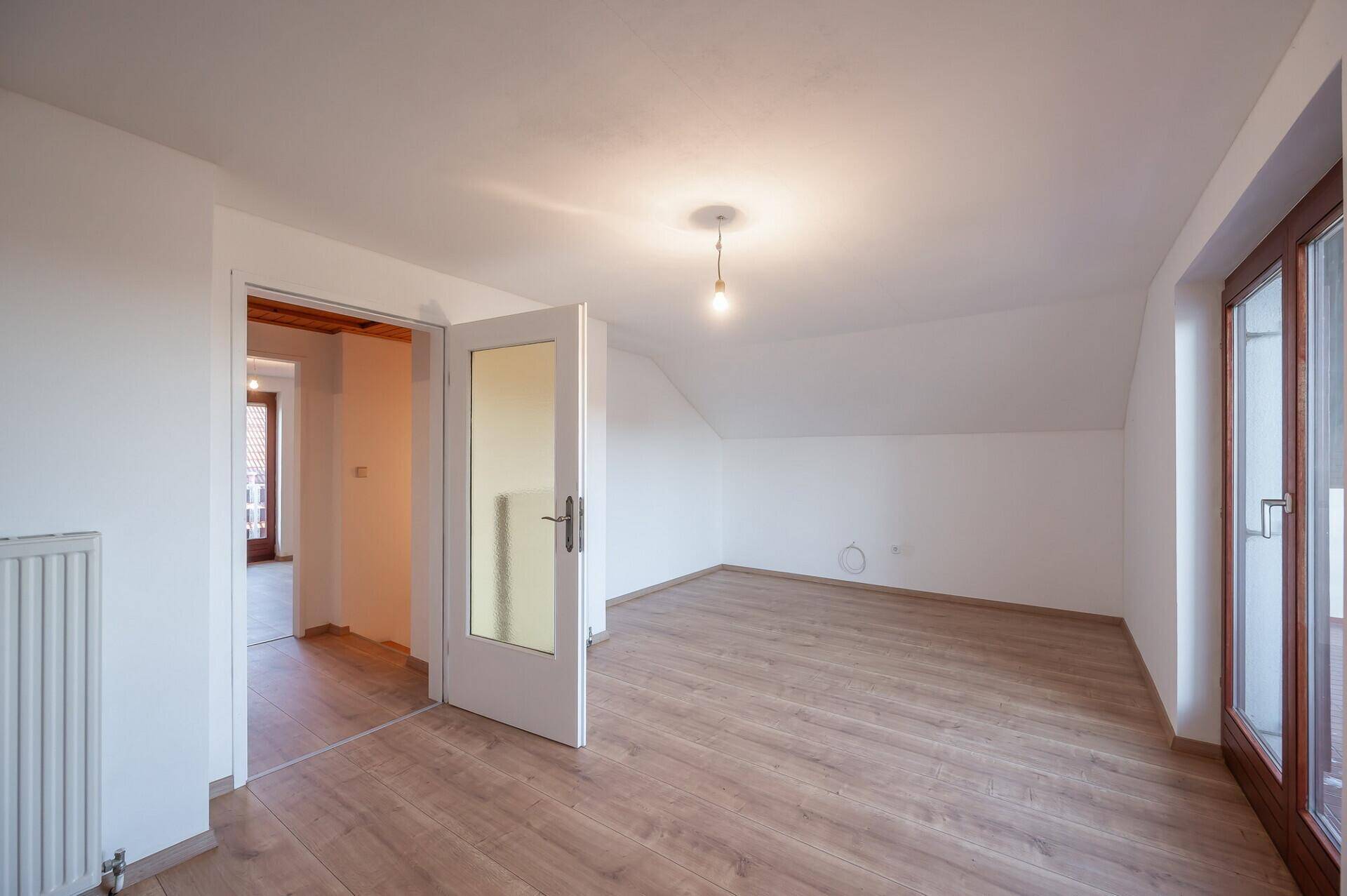 Geräumiges Zimmer im Dachgeschoss mit Schrägen, Laminatboden und Zugang zu einem Balkon.