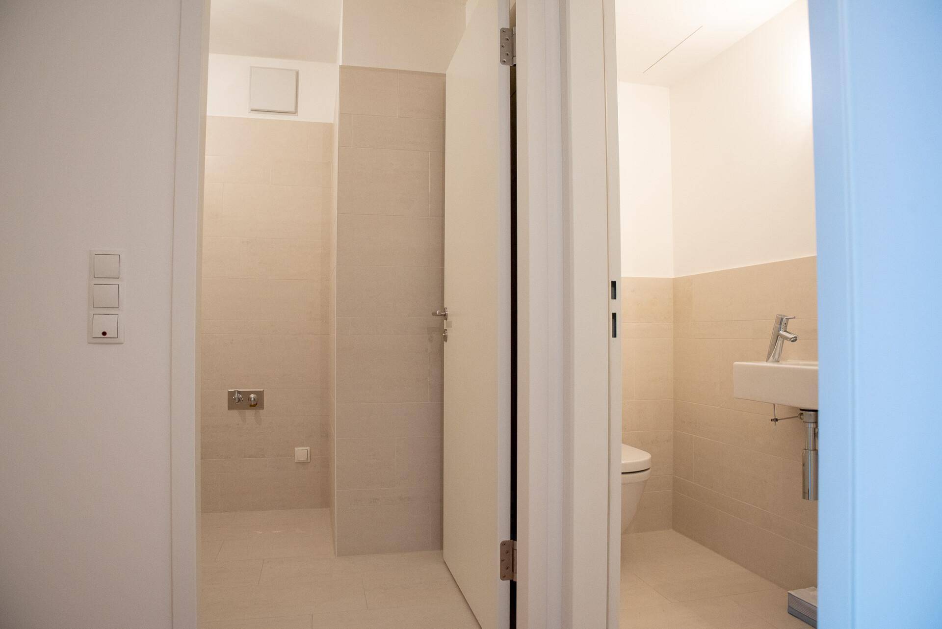 Modernes Badezimmer mit beigefarbenen Fliesen, separatem WC und Duschbereich.