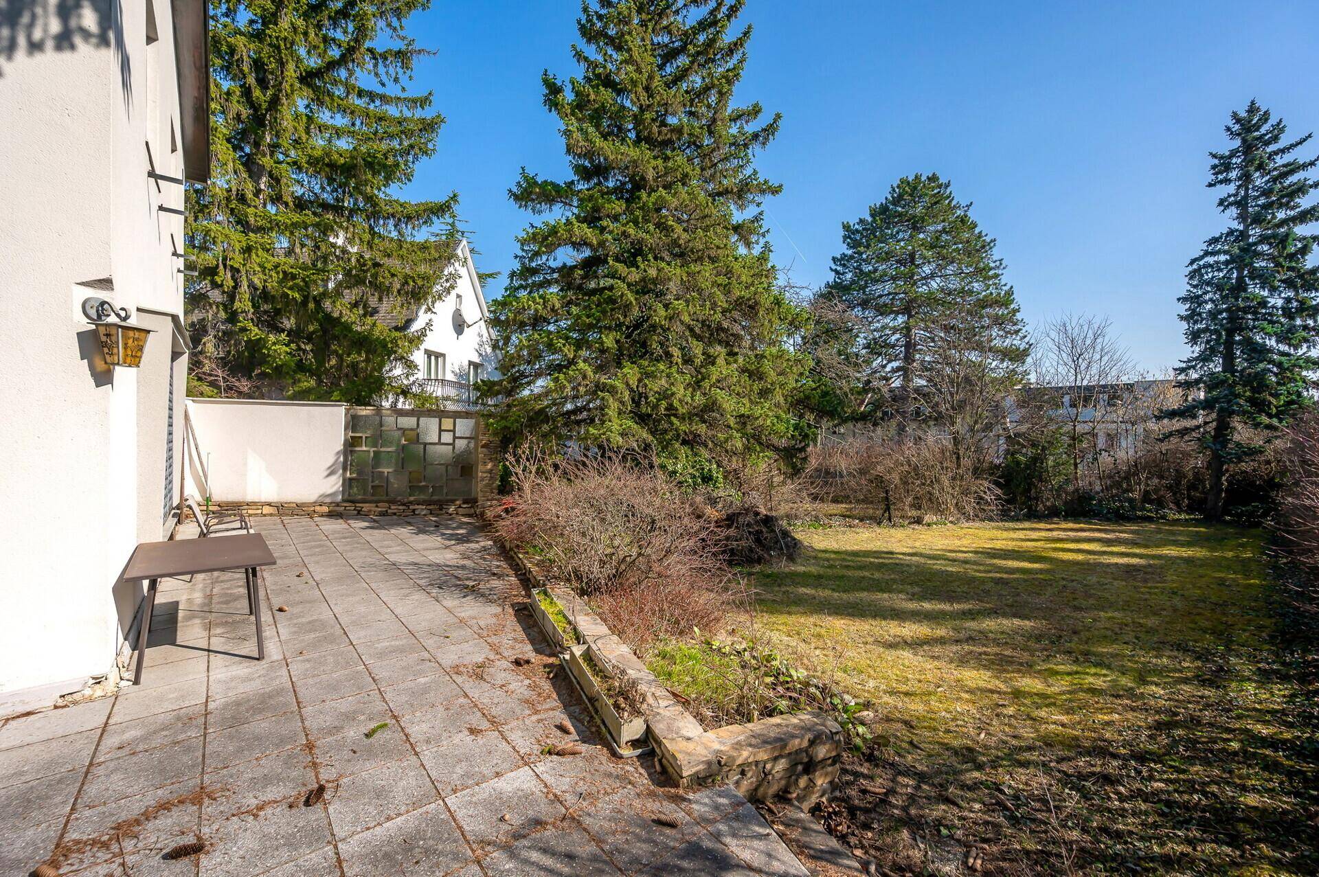 Gepflasterte Terrasse mit Sitzgelegenheiten und Blick auf den weitläufigen Garten mit Bäumen.