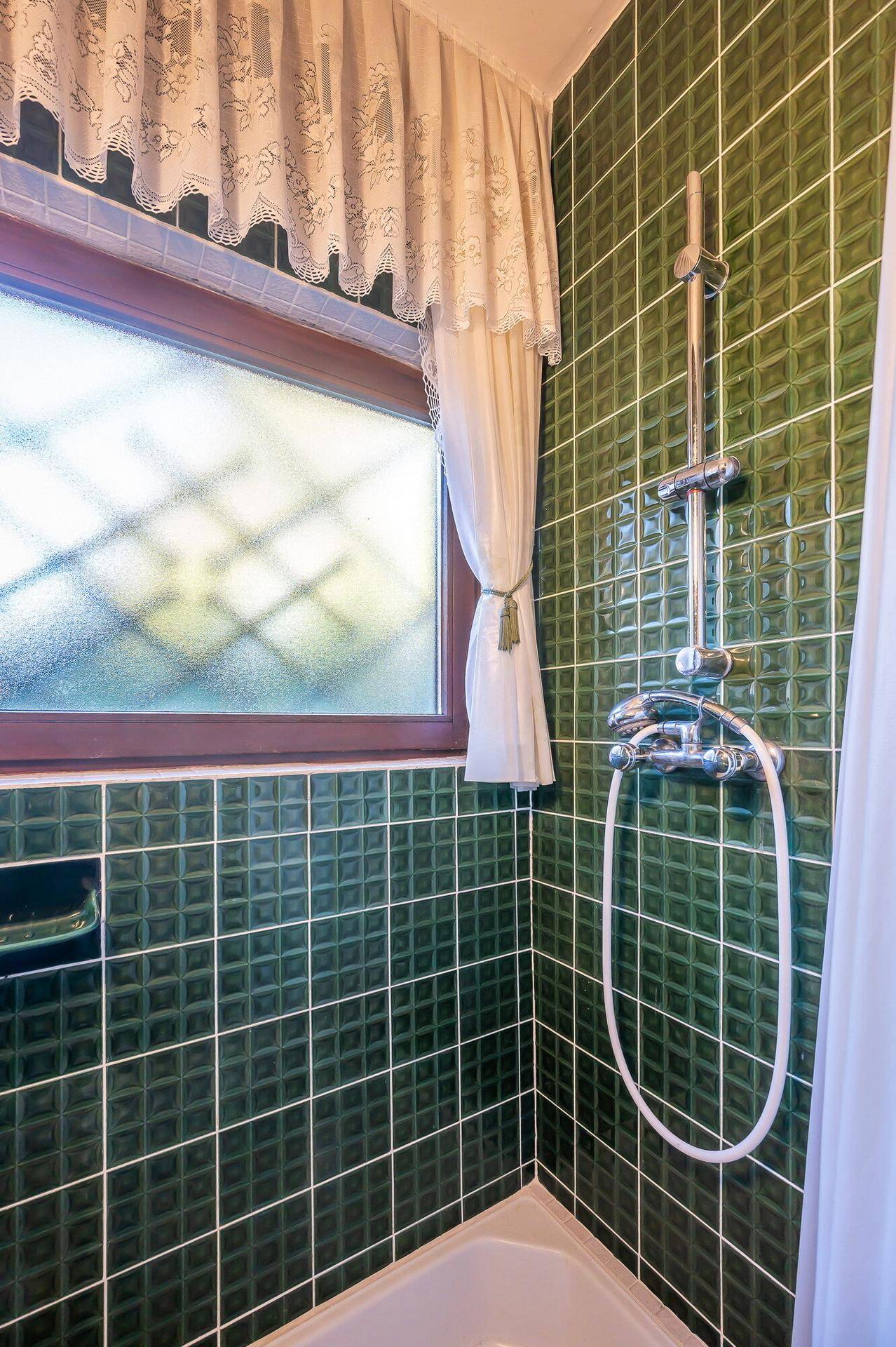 Duschbereich im Badezimmer mit grünen Fliesen und Fenster, im älteren Stil.