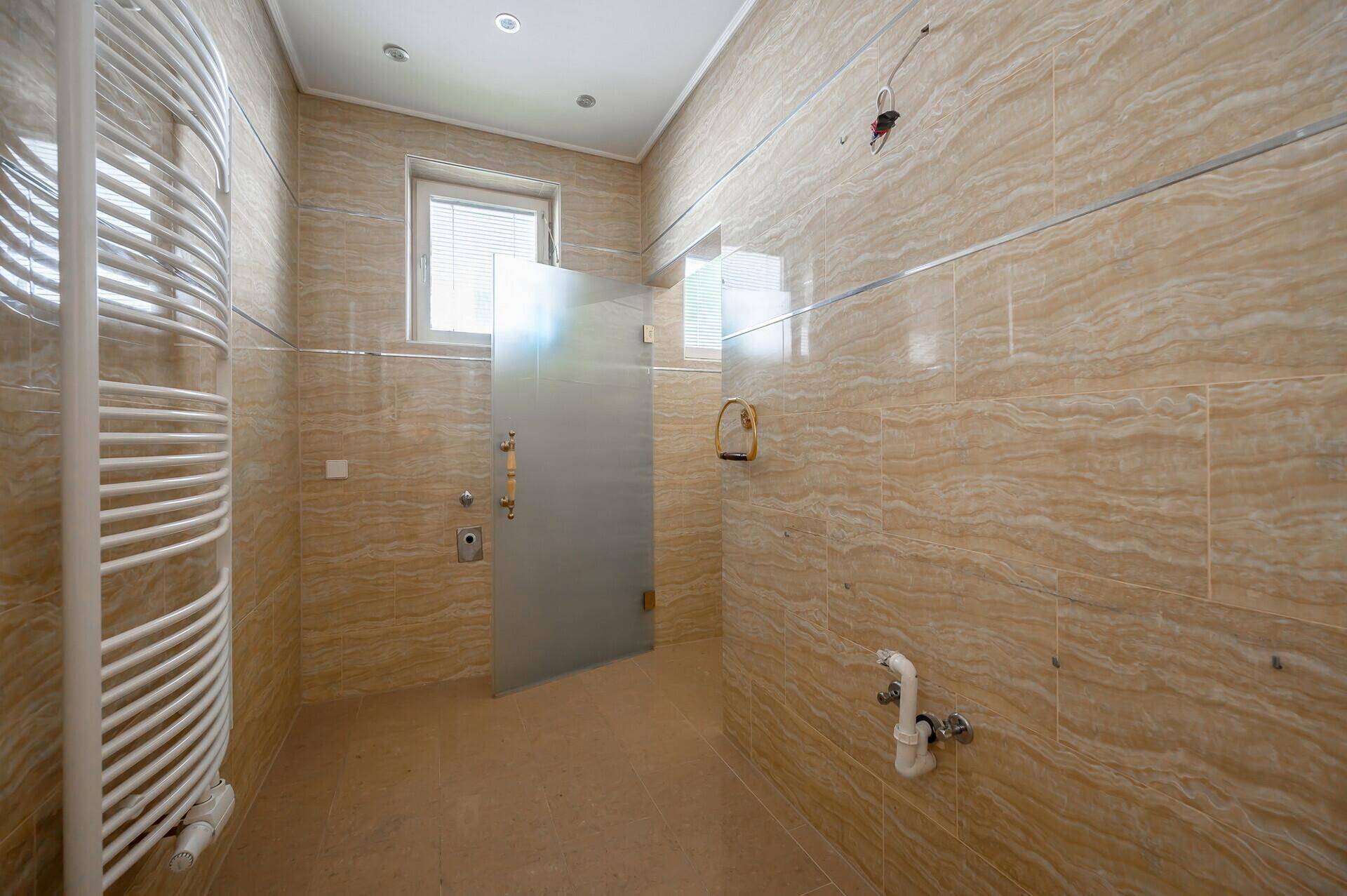 Modernes Badezimmer mit beigen Fliesen, Fenster und beheiztem Handtuchhalter.
