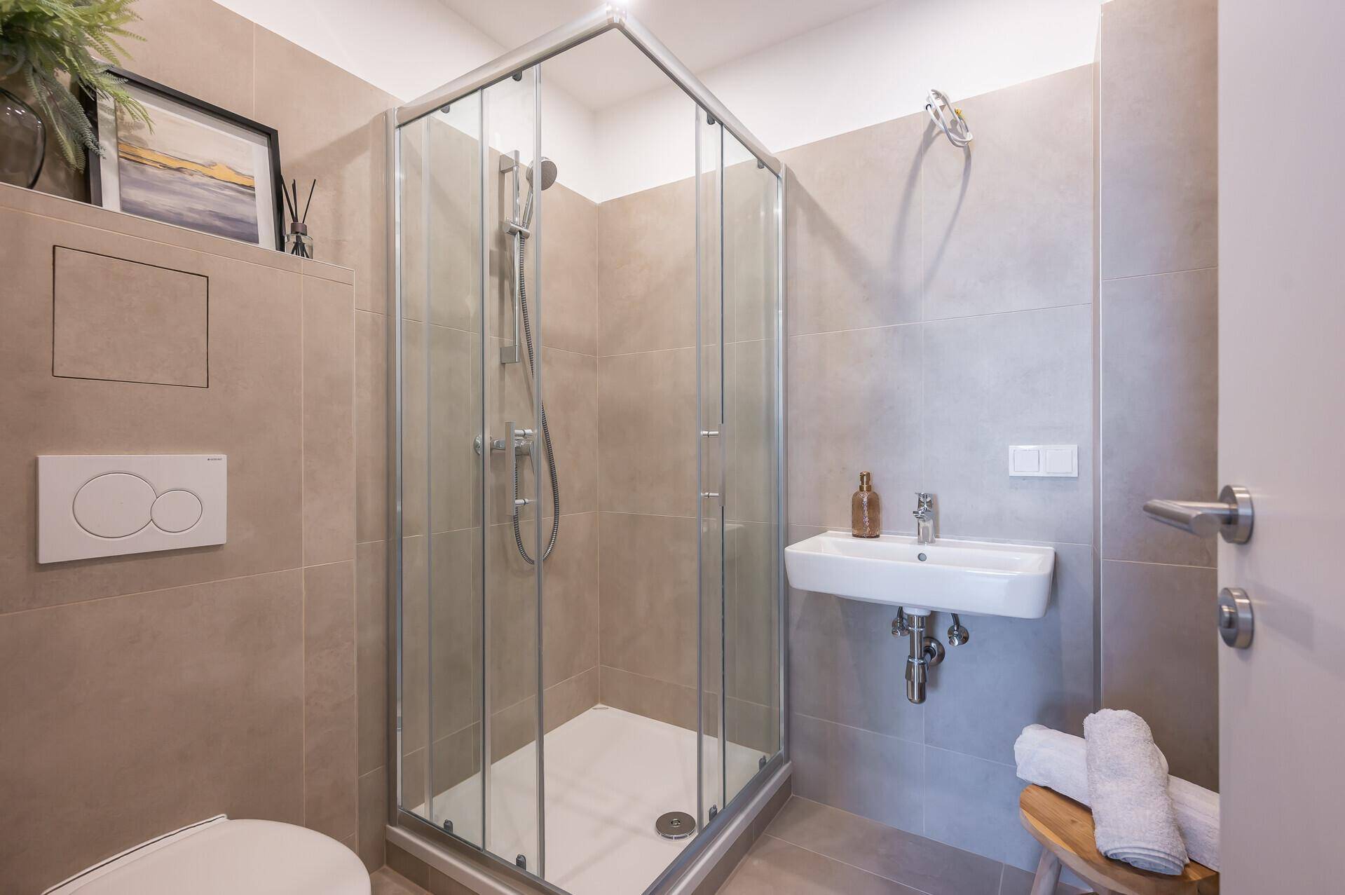 Modernes Badezimmer mit Duschkabine, Wand-WC und kleinem Waschbecken.