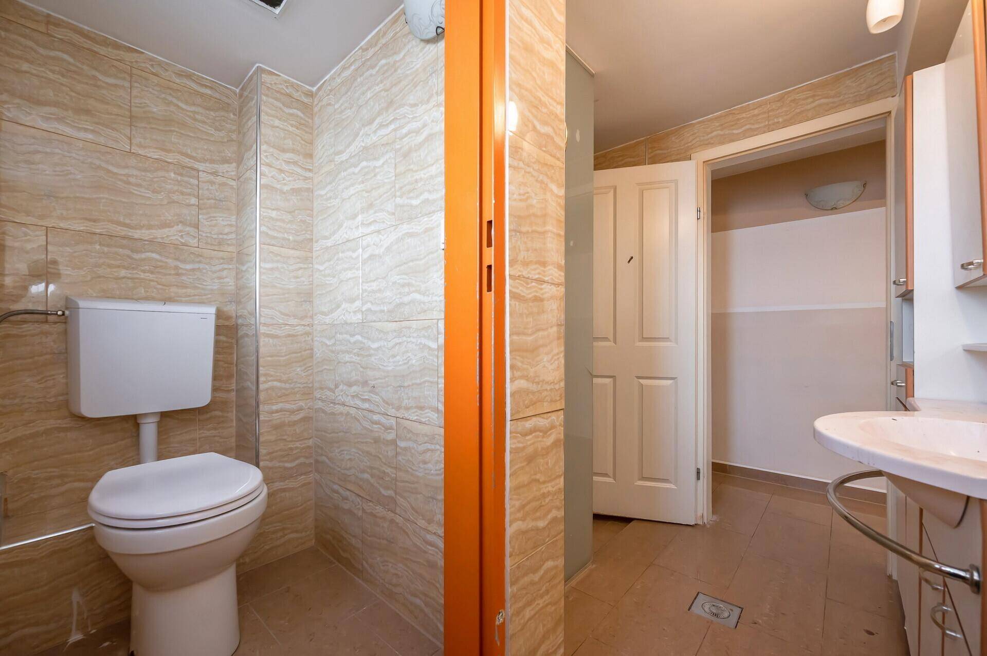 Badezimmer mit Toilette, Waschtisch und beigefarbenen Wandfliesen.