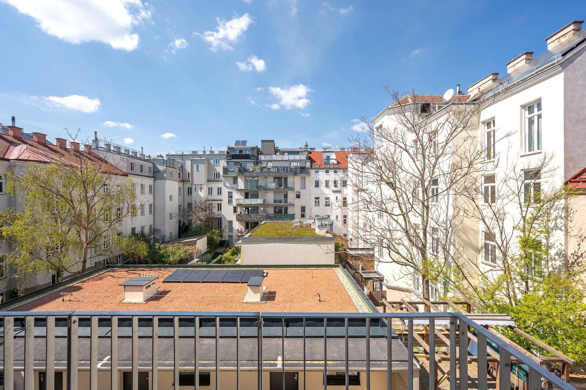 Aussicht vom Balkon auf Dächer mit Solarpaneelen und die umliegende Wohnbebauung unter blauem Himmel.