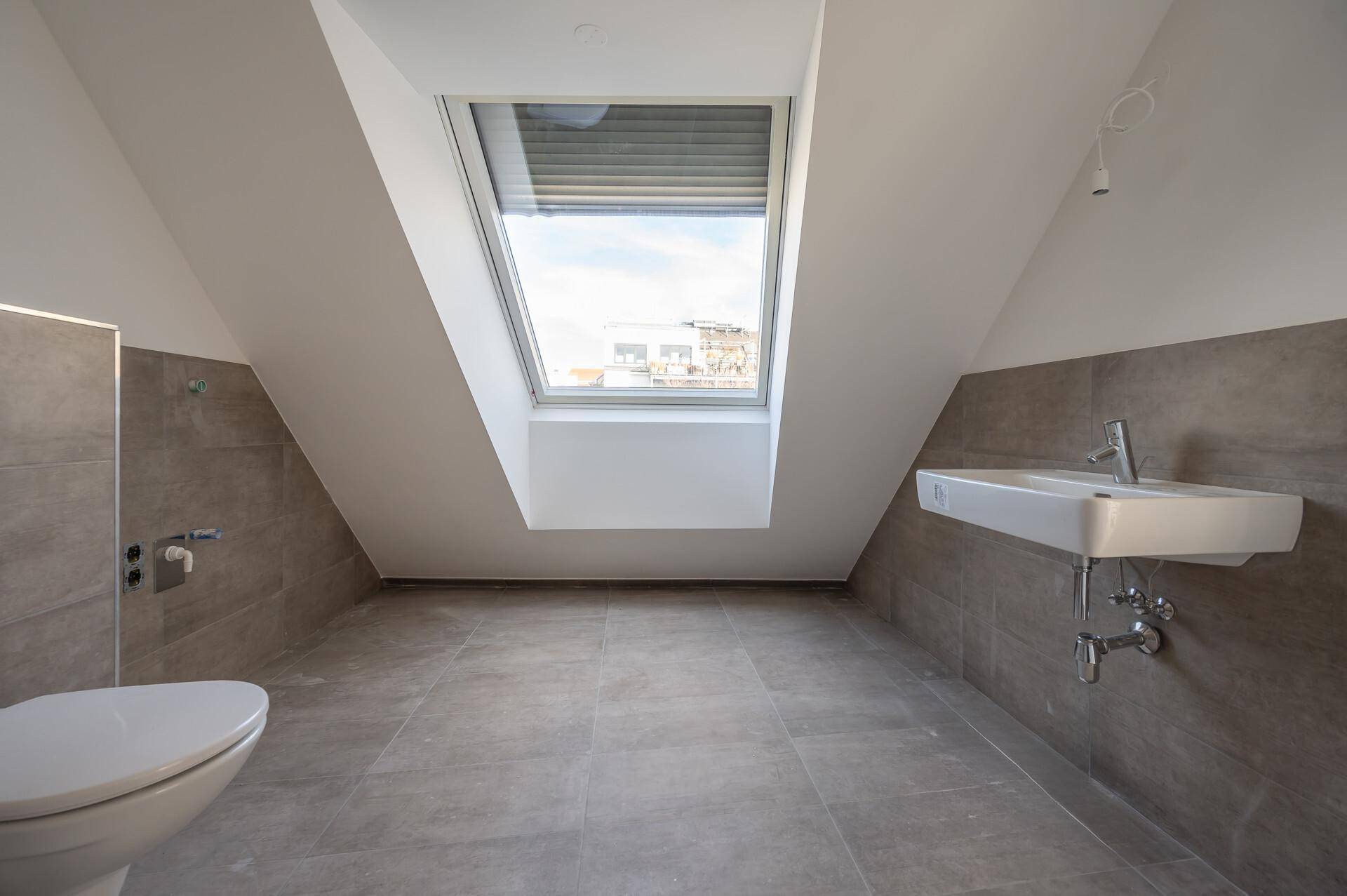 Helles Badezimmer mit Dachschräge, Dachfenster und modernen grauen Fliesen.