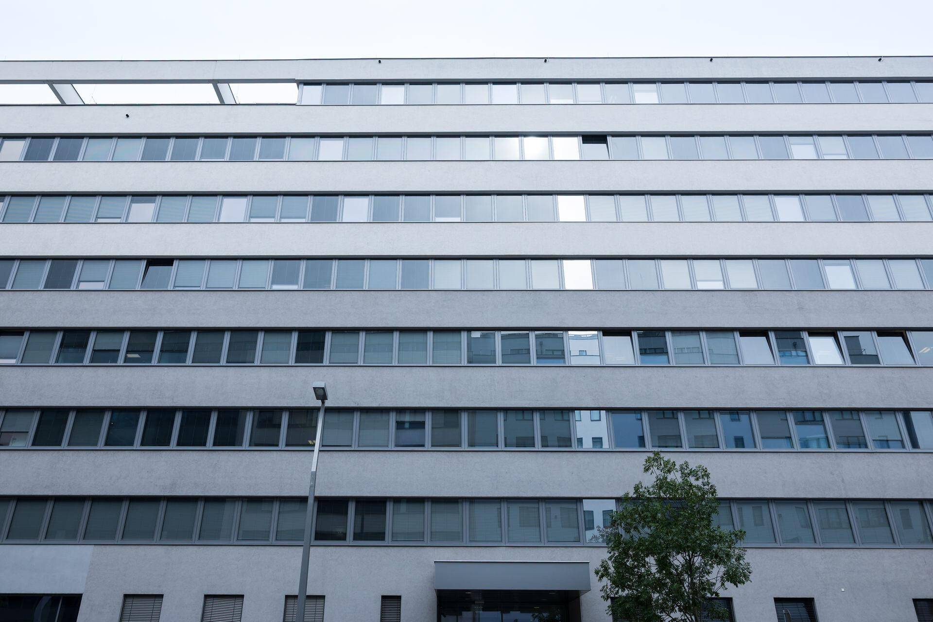 Fassade eines modernen Gebäudes mit vielen horizontalen Fensterreihen unter einem bewölkten Himmel.