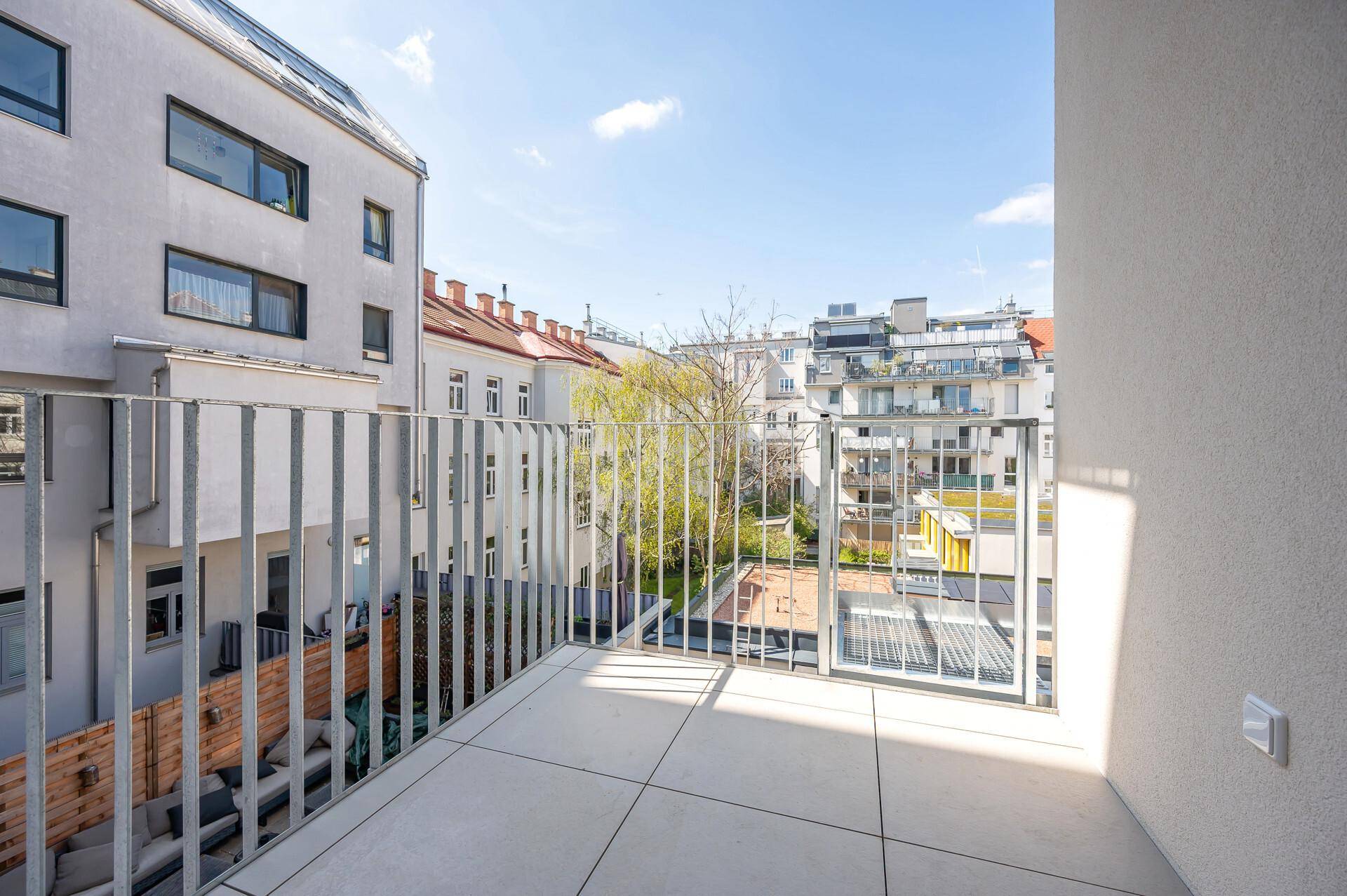Geräumiger Balkon mit hellen Fliesen und Metallgeländer, bietet Blick auf die umliegenden Gebäude.