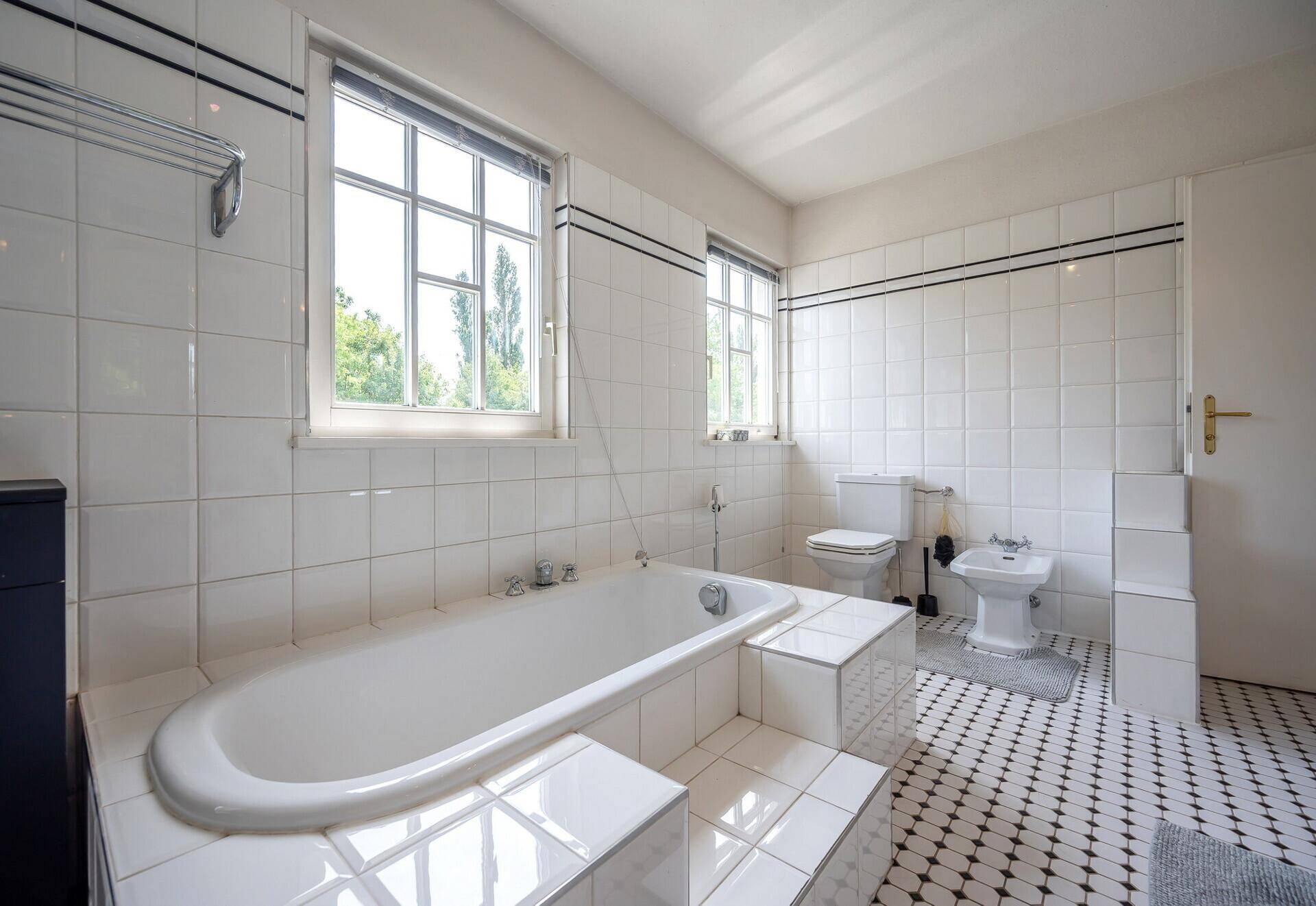 Helles Badezimmer mit Badewanne, WC, Bidet und zwei Fenstern für viel Licht.