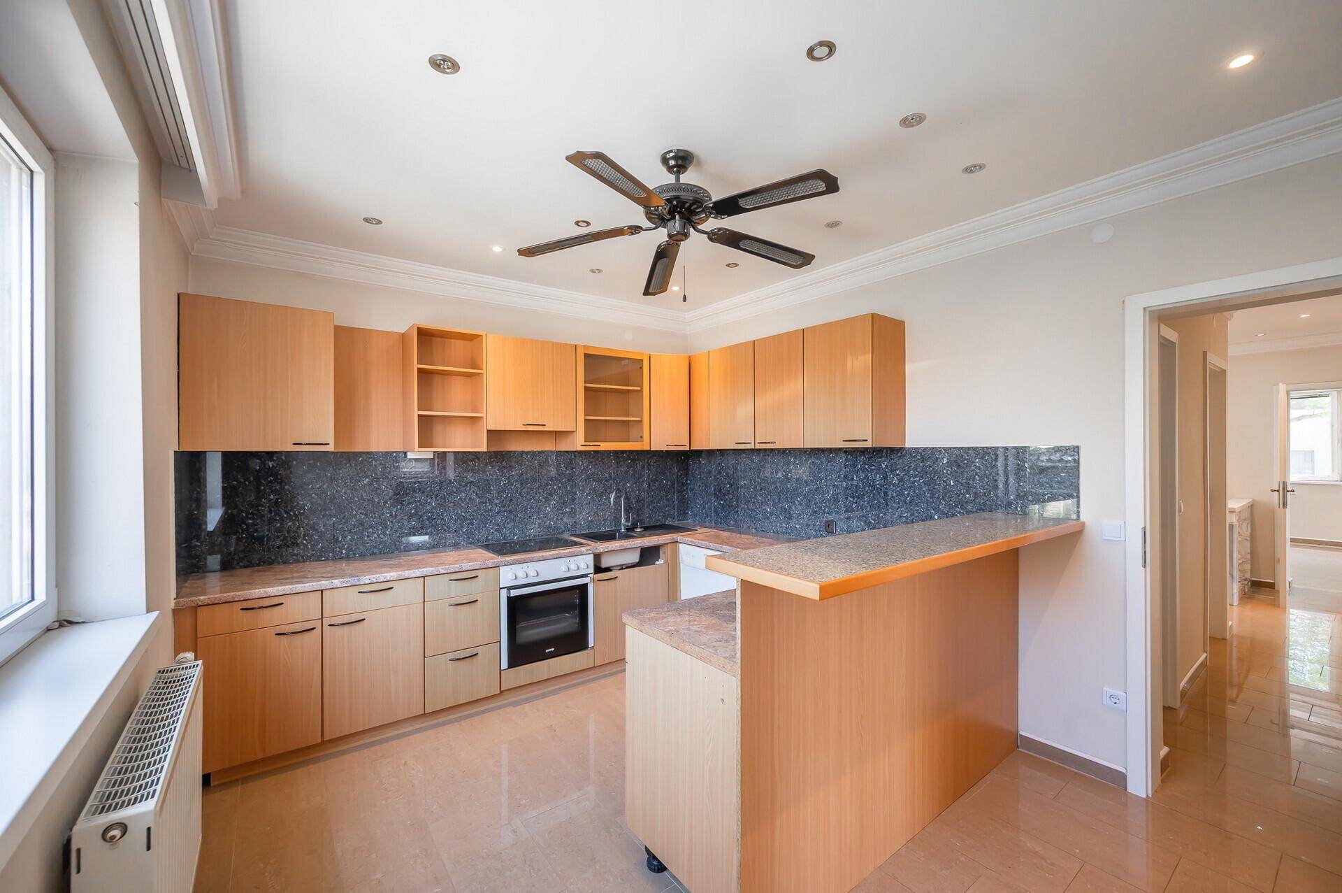 Funktionale Küche mit Holzschränken, Granitarbeitsplatten und Deckenventilator.