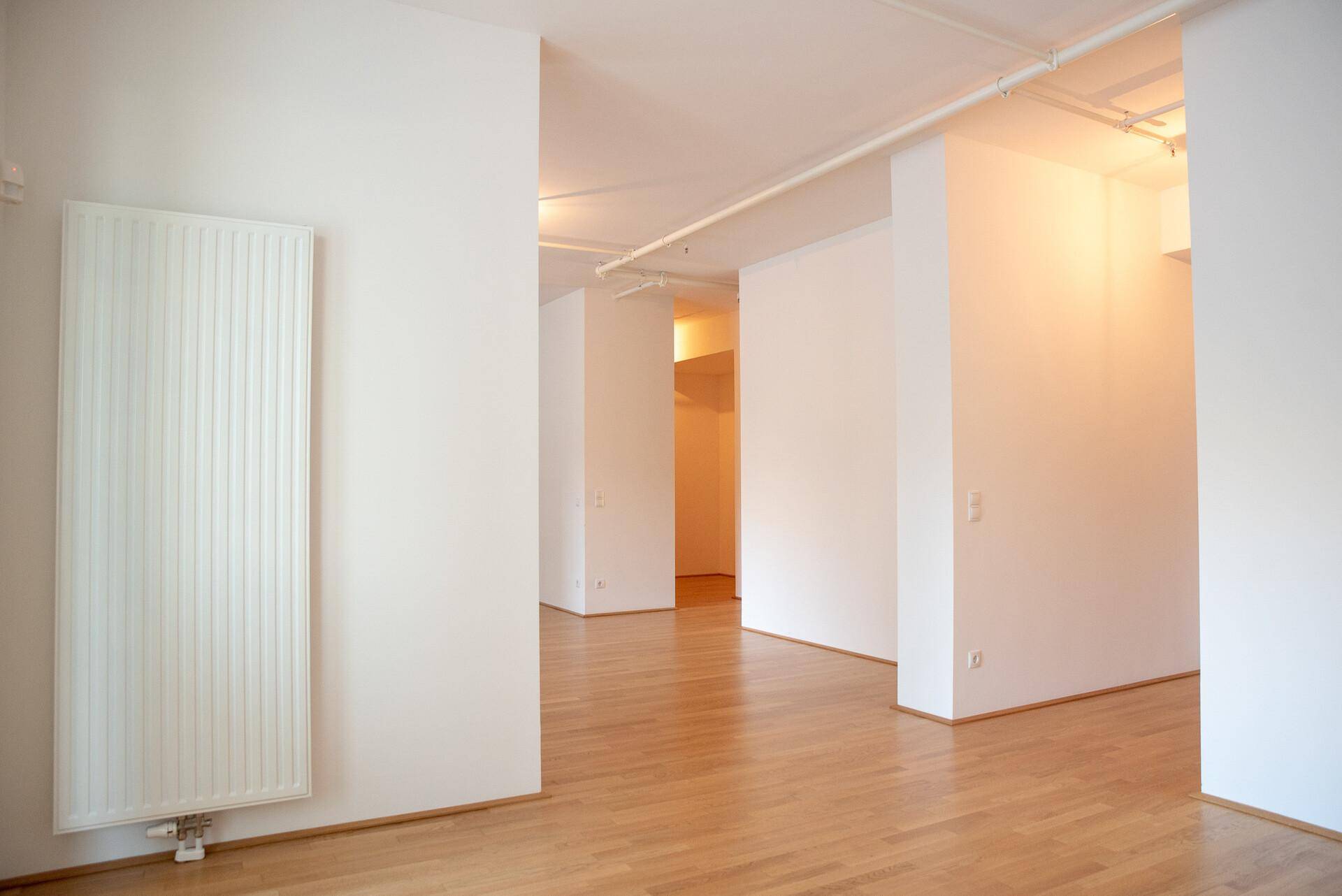 Langer, heller Flur mit Holzboden und sichtbaren Deckenleitungen, führt durch die Wohnung.