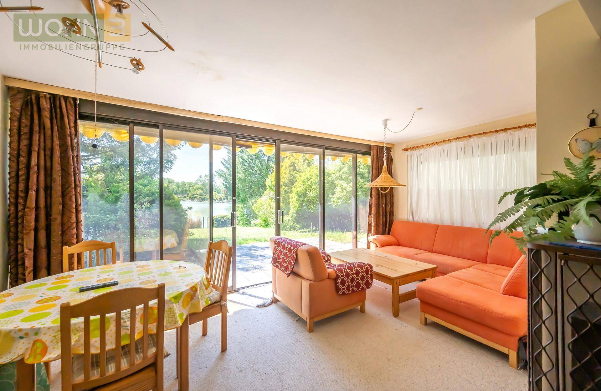 Gemütlicher Wohn-Essbereich mit orangefarbenem Sofa und großzügigen Schiebetüren zum Garten.