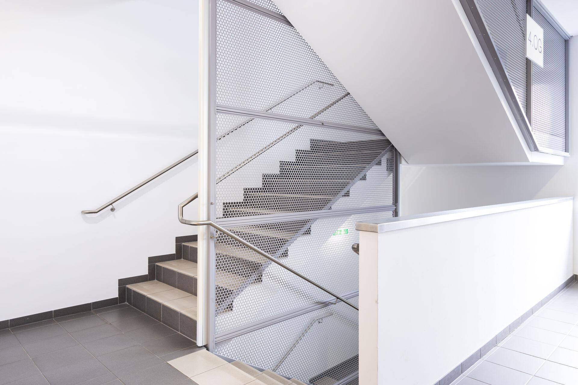 Modernes Treppenhaus mit Metallgeländer und perforierten Wänden, das mehrere Etagen verbindet.