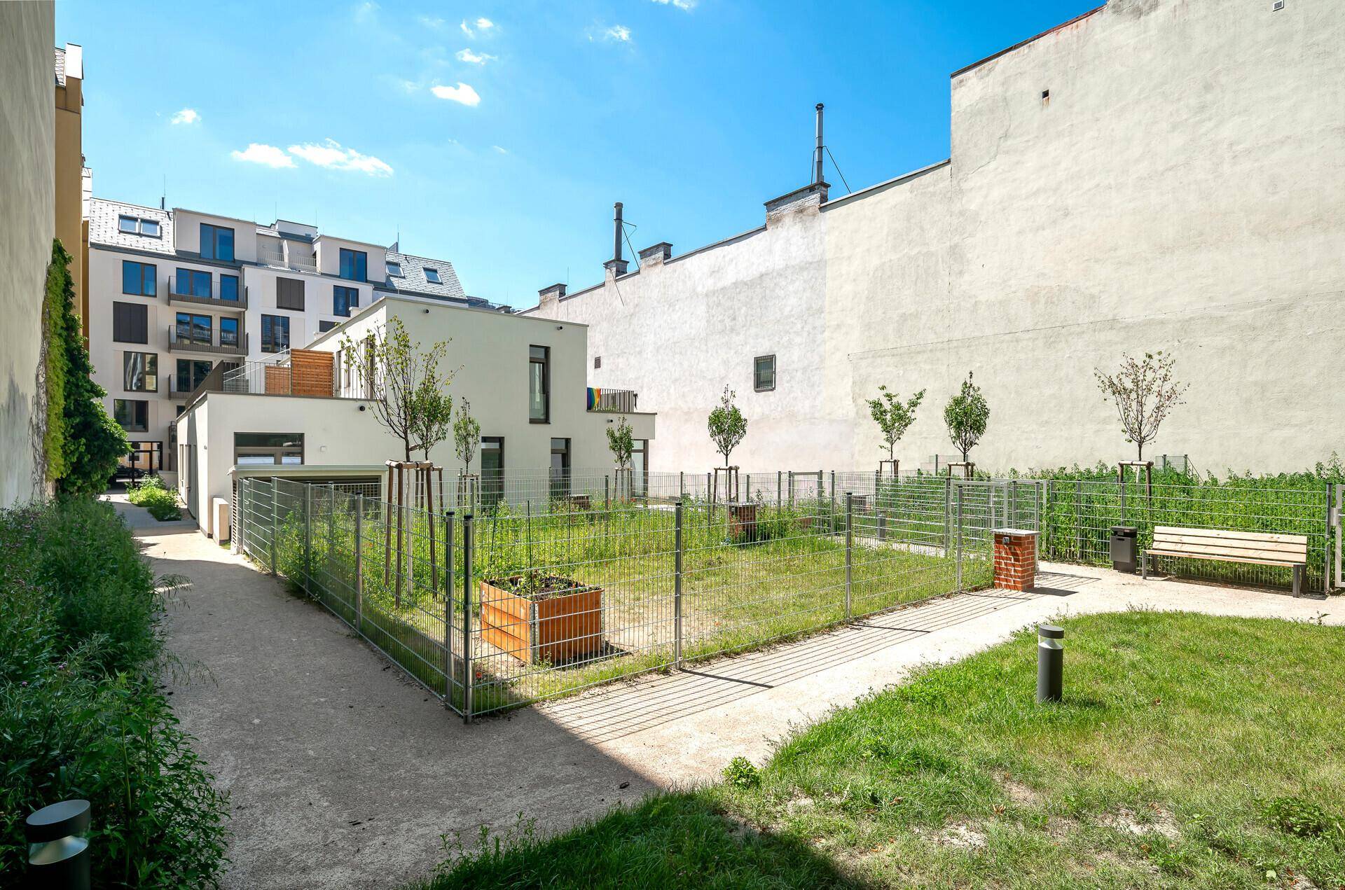 Gemeinschaftlicher Gartenbereich mit Rasenfläche und Sitzbank zwischen Gebäuden.