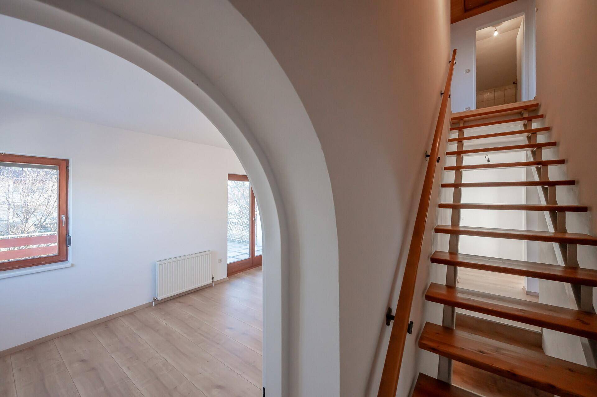Heller Flur mit Holztreppe und einem Rundbogen, der zum Wohnbereich führt.