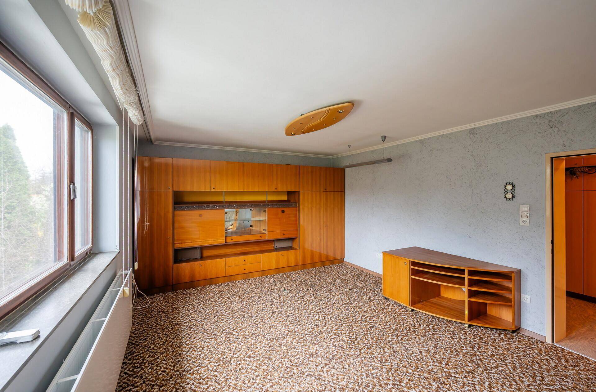 Geräumiges Wohnzimmer mit gemustertem Teppichboden und einer großen Holzschrankwand.