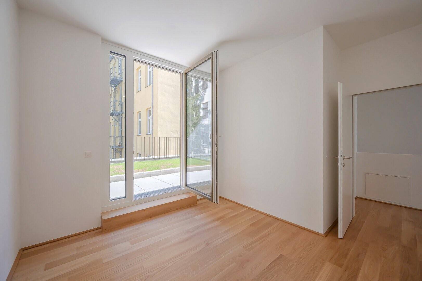 Heller Raum mit Holzboden und großen Fenstern, die Zugang zum Außenbereich bieten.