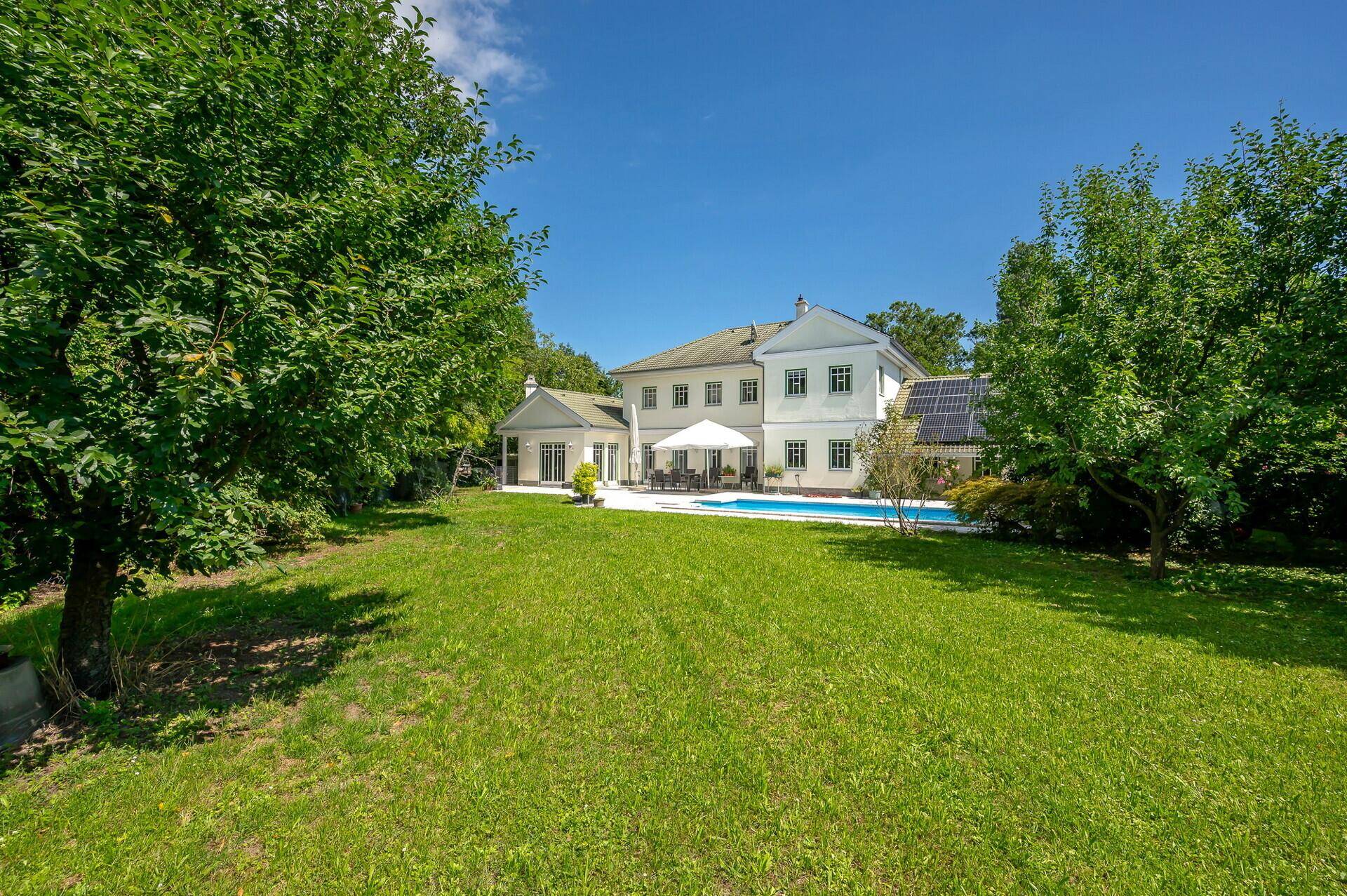 Weitläufiger Garten mit altem Baumbestand und Blick auf die Villa mit Pool.
