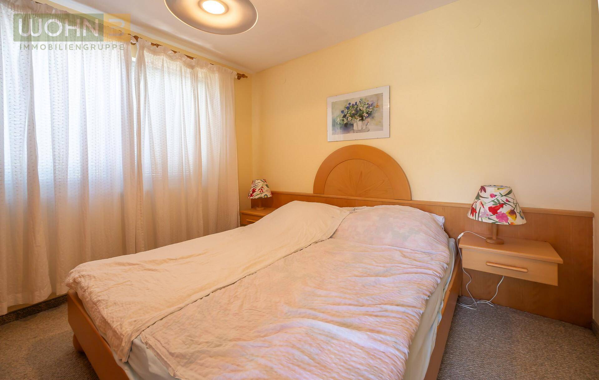 Gemütliches Schlafzimmer mit Doppelbett, Holzmöbeln und einem Fenster mit hellen Vorhängen.