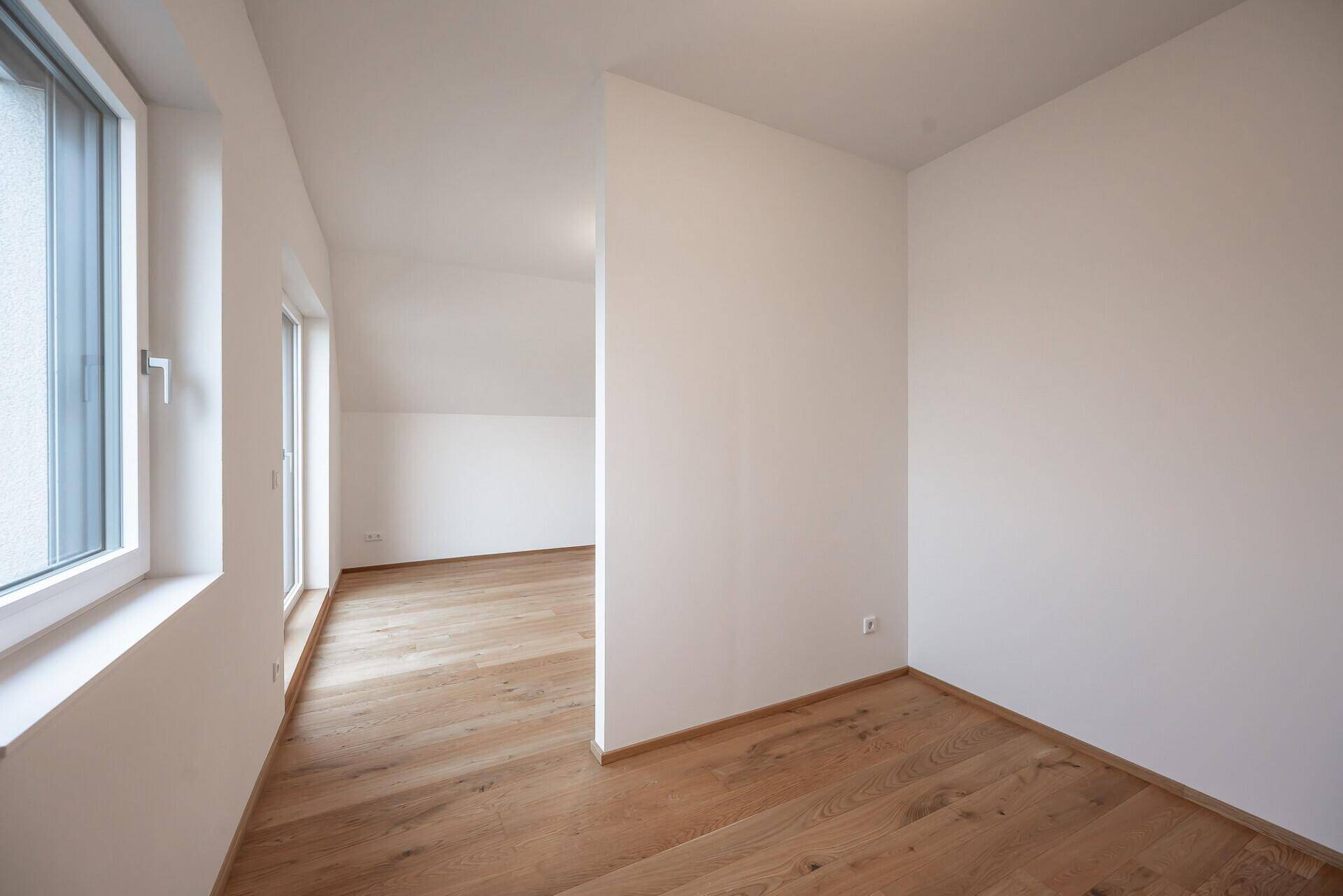 Helles Schlafzimmer im Dachgeschoss mit Holzboden und schrägen Wänden.