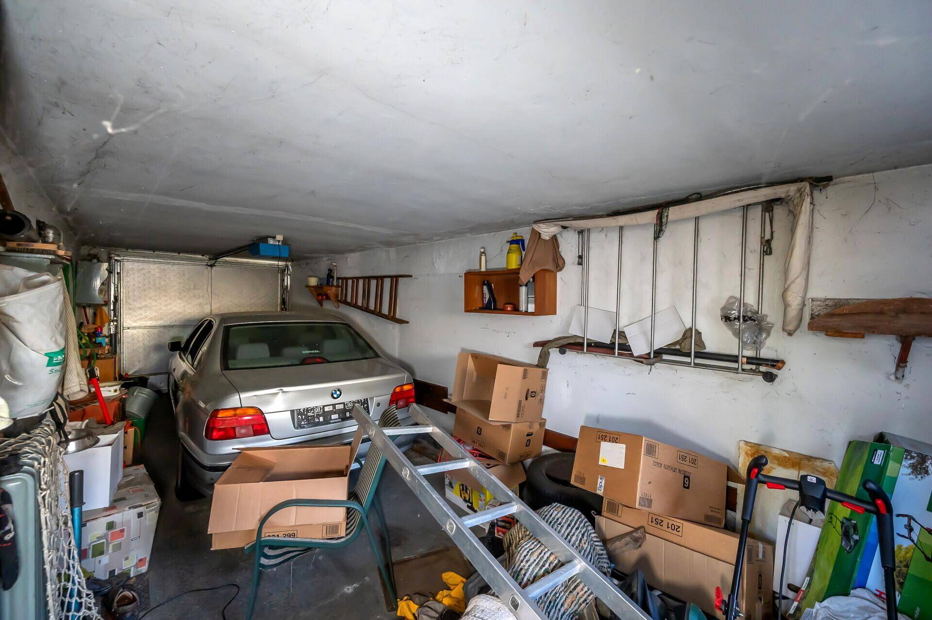 Geräumige Garage mit einem geparkten Auto, gefüllt mit Kartons und verschiedenen Lagergegenständen.