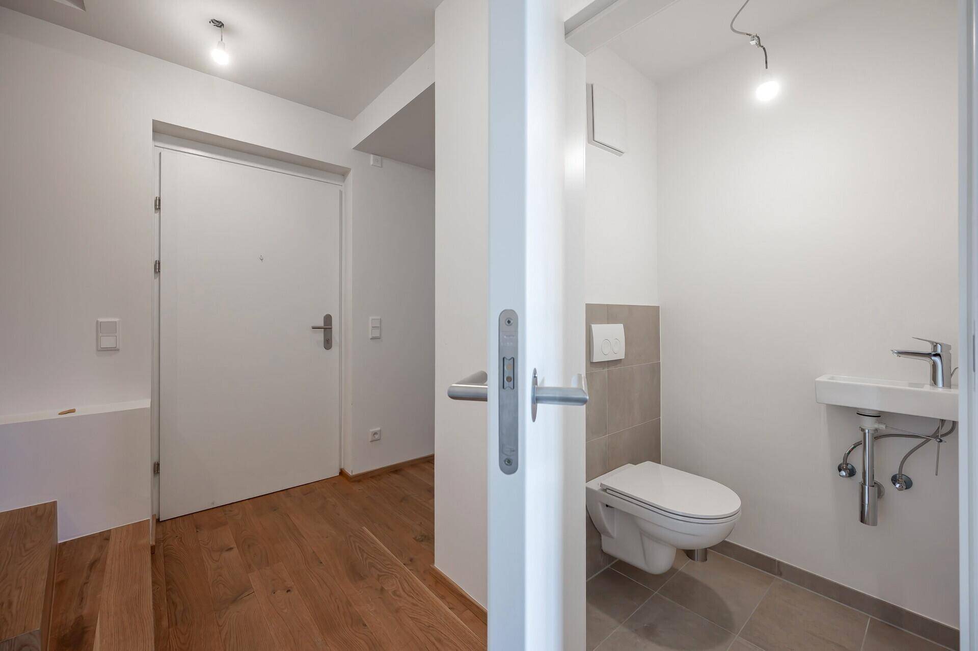 Modernes Gäste-WC mit Wand-WC, kleinem Waschbecken und Fliesenboden in neutralen Farben.